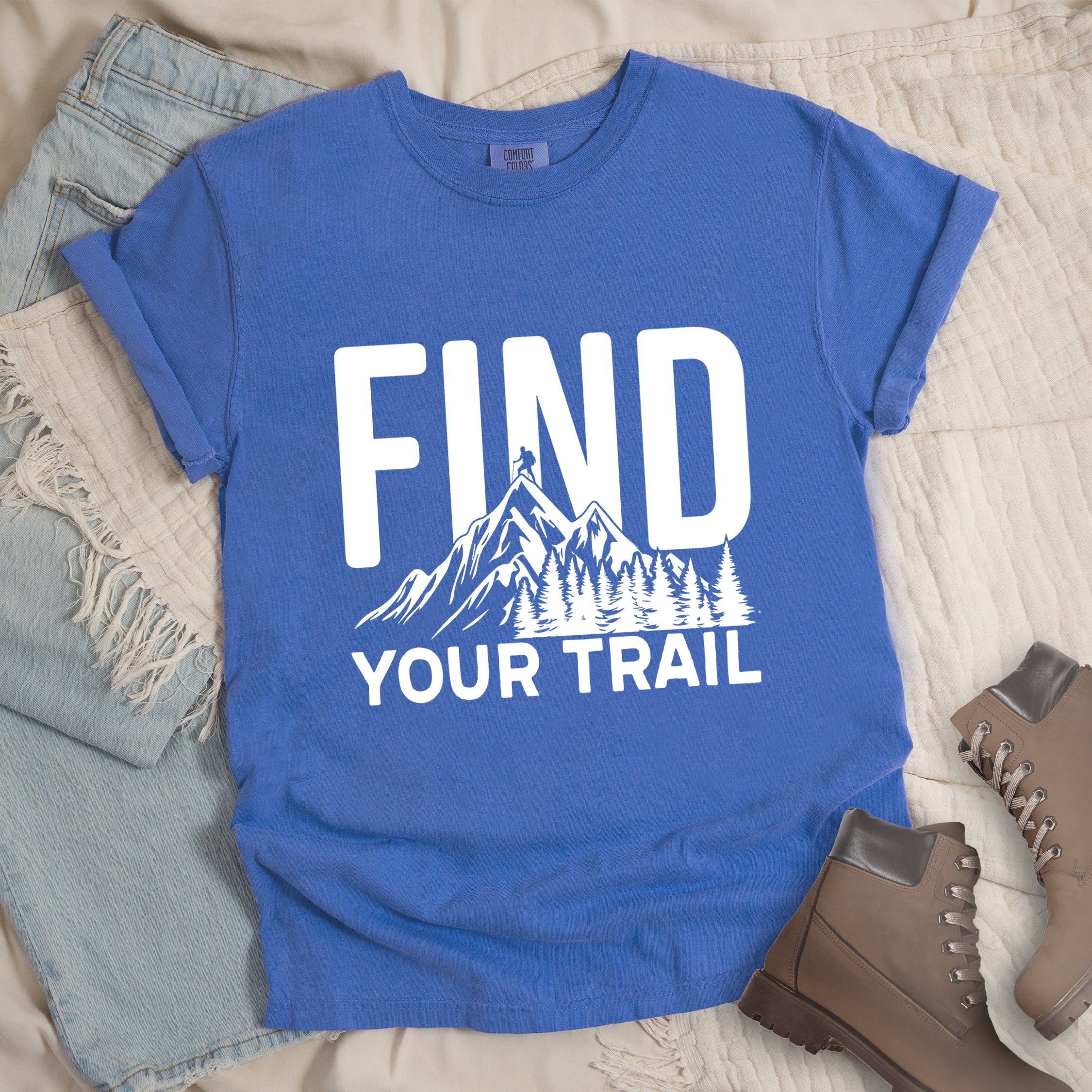Flo Blue (Bright Blue) graphic t-shirt with 'Find Your Trail' text and white mountain and forest design, styled with light wash jeans and brown hiking boots