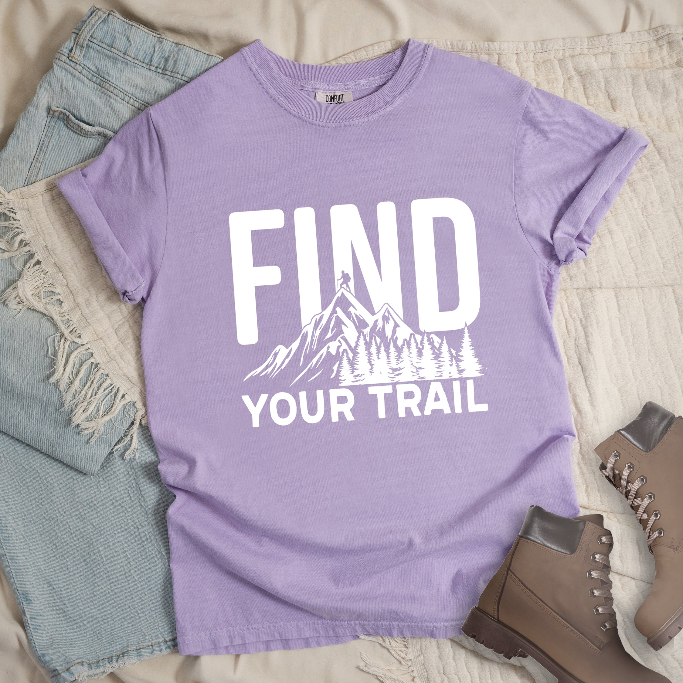 Orchid (Light Violet) graphic t-shirt with 'Find Your Trail' text and white mountain and forest design, styled with light wash jeans and brown hiking boots