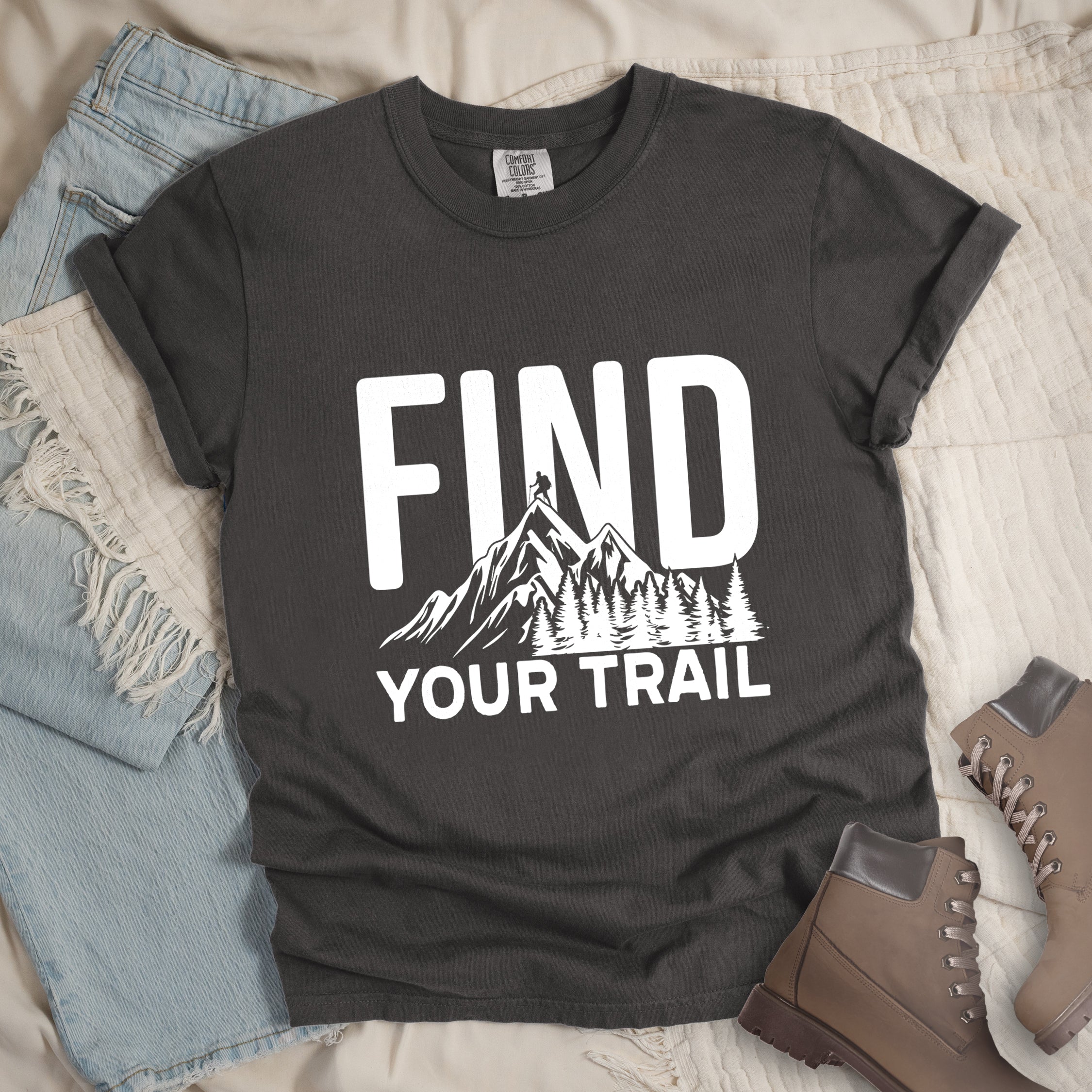 Pepper (Dark Gray) graphic t-shirt with 'Find Your Trail' text and white mountain and forest design, styled with light wash jeans and brown hiking boots