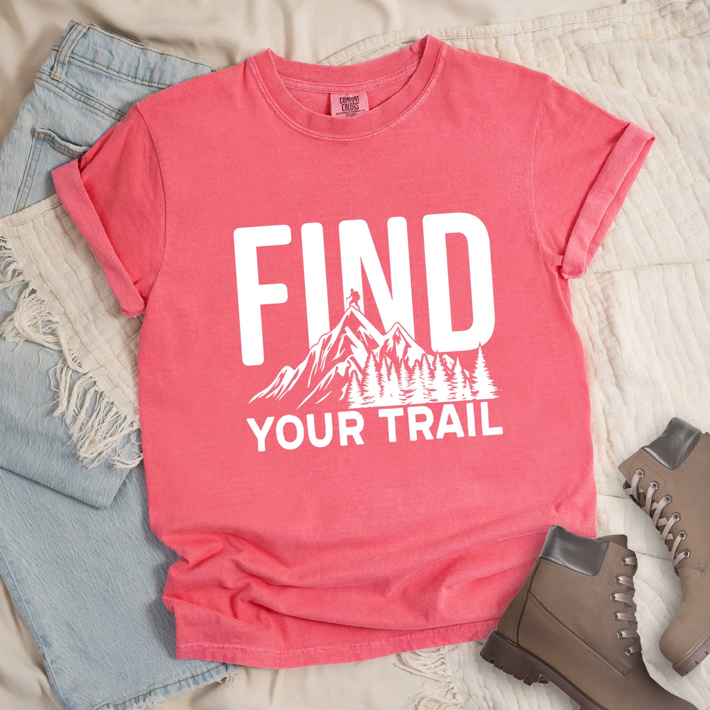 Watermelon (Light Coral) graphic t-shirt with 'Find Your Trail' text and white mountain and forest design, styled with light wash jeans and brown hiking boots