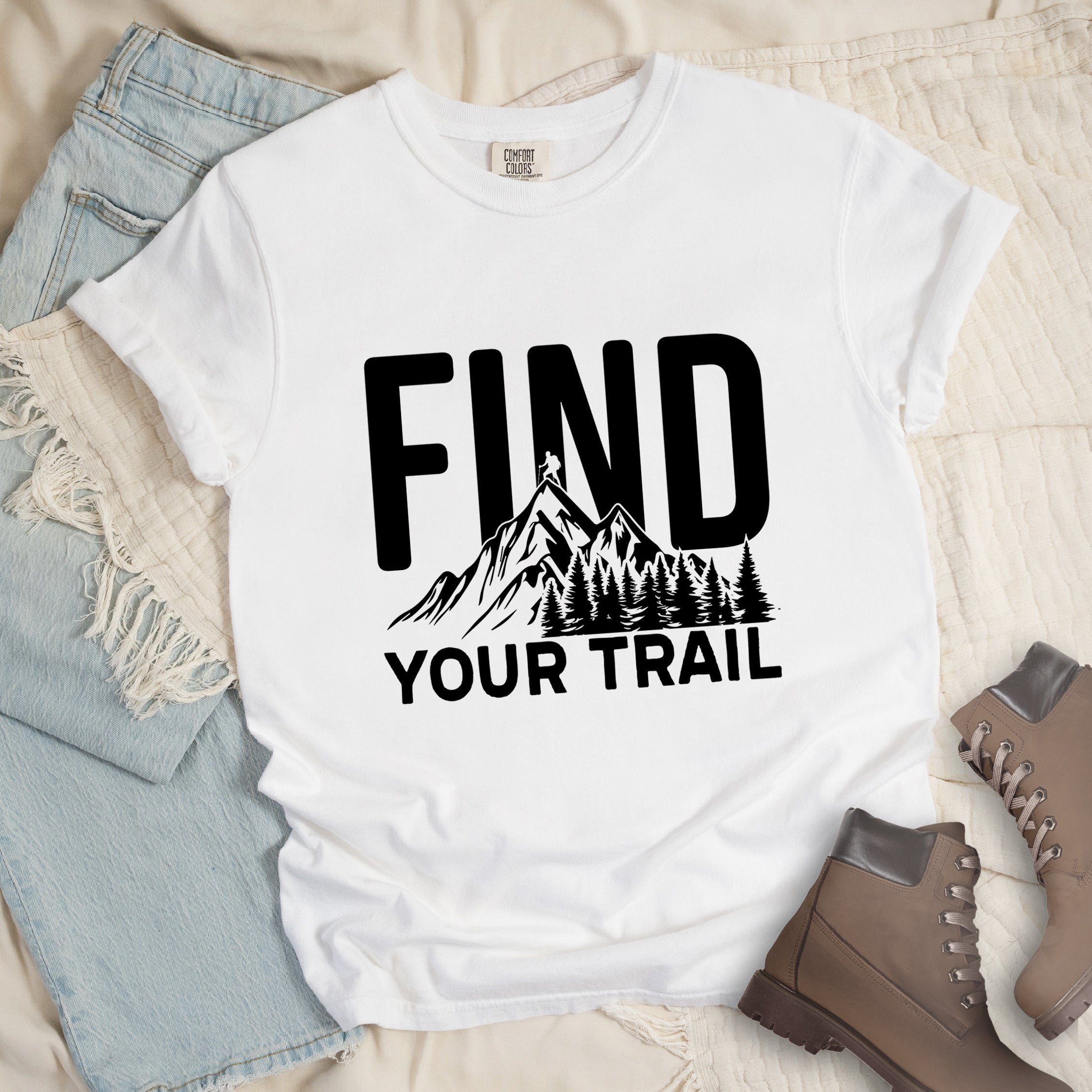 White graphic t-shirt with 'Find Your Trail' text and black mountain and forest design, styled with light wash jeans and brown hiking boots