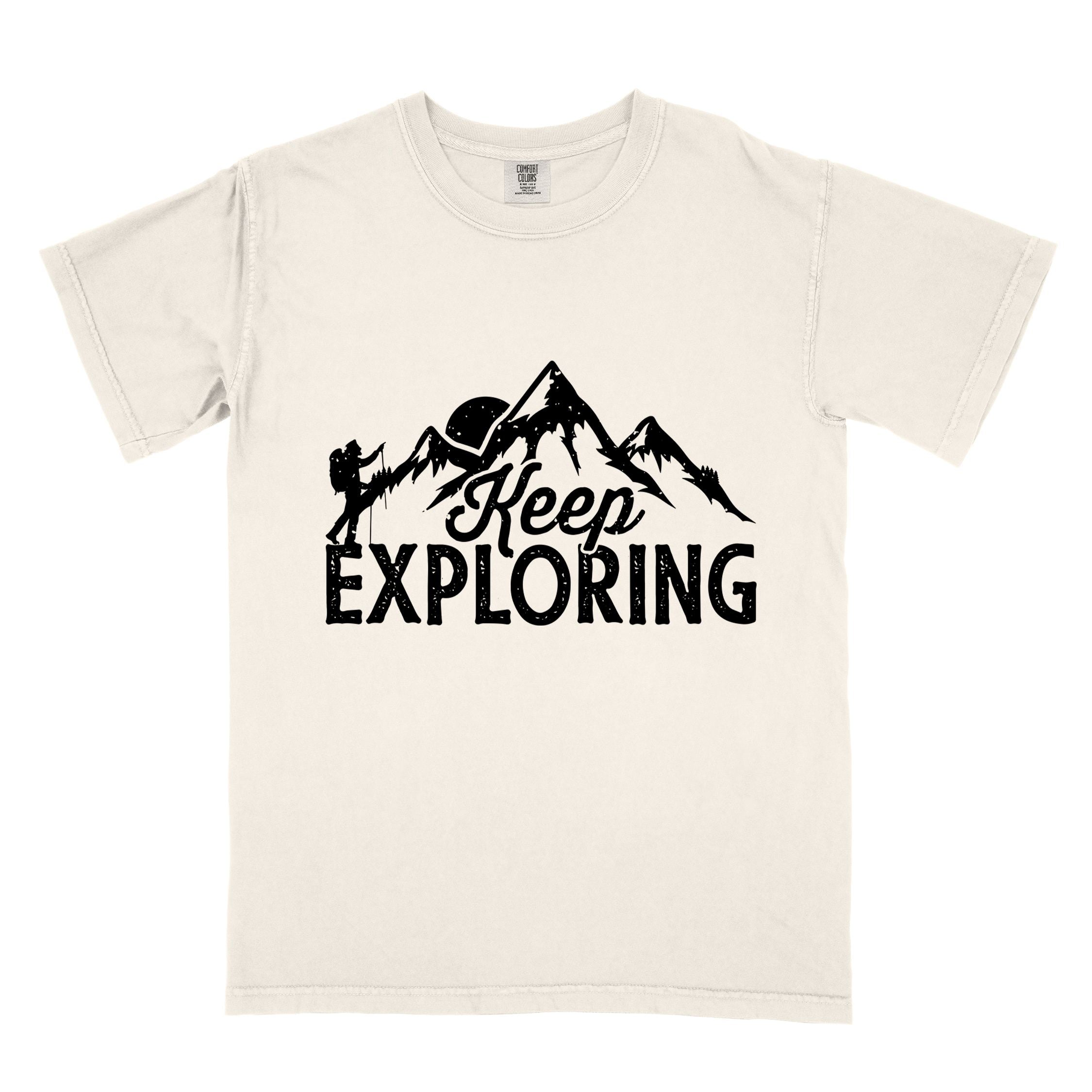 Ivory "Keep Exploring" colored statement tee with bold typography, mountains, birds, perfect for adventure motivated individuals.