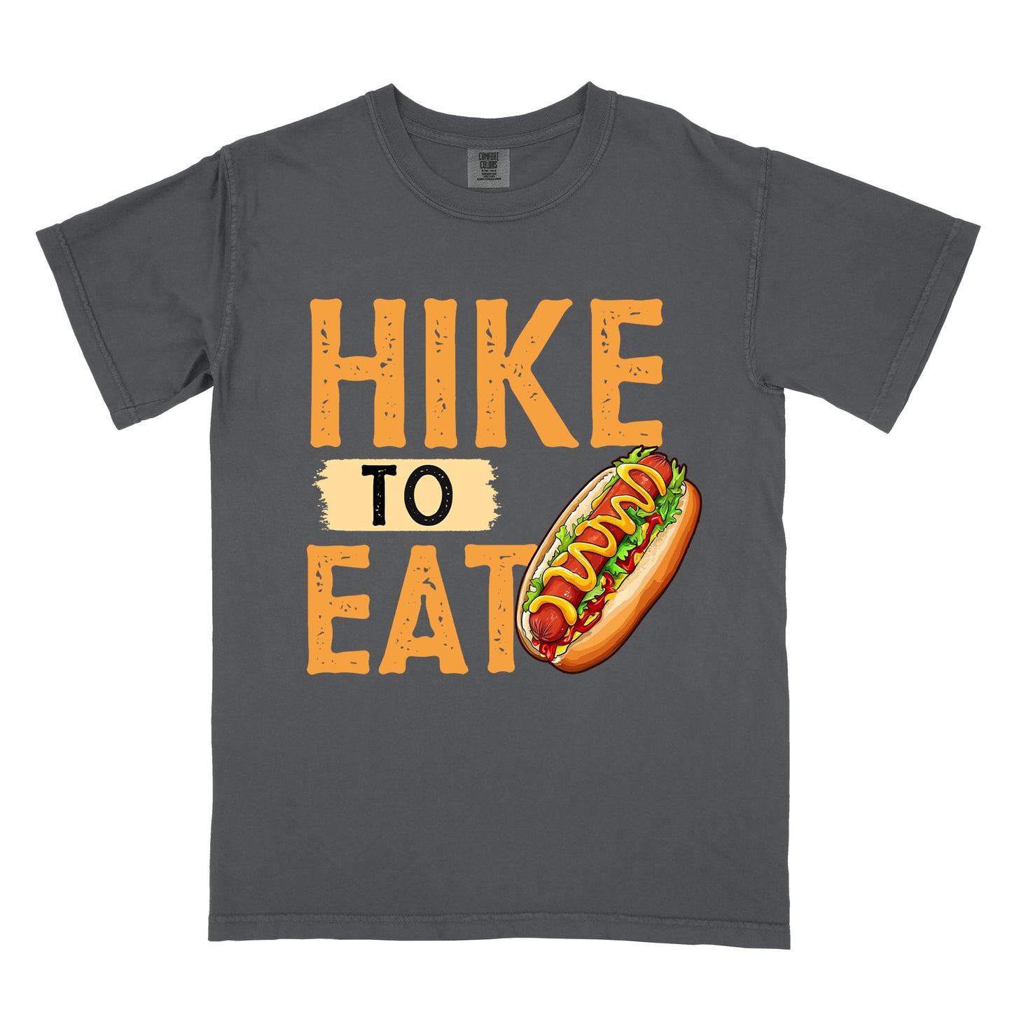 Graphite (Deep Gray) t-shirt with "HIKE TO EAT" in distressed orange lettering. The word "TO" appears on a beige background between "HIKE" and "EAT". A colorful hot dog illustration with mustard, ketchup and toppings appears next to the "T" in "EAT".