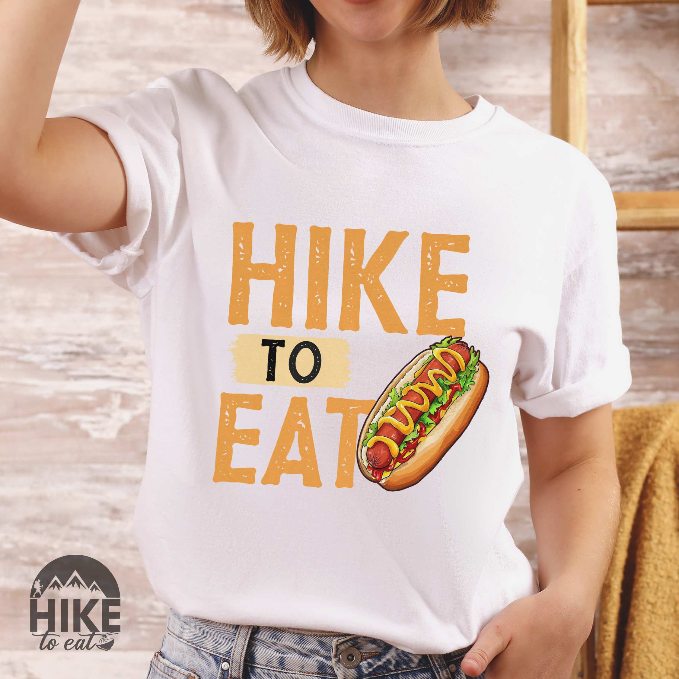 Woman wearing white "Hike to Eat" colored vintage tee with bold typography, and illustrated hotdog with mustard and ketchup sauce.