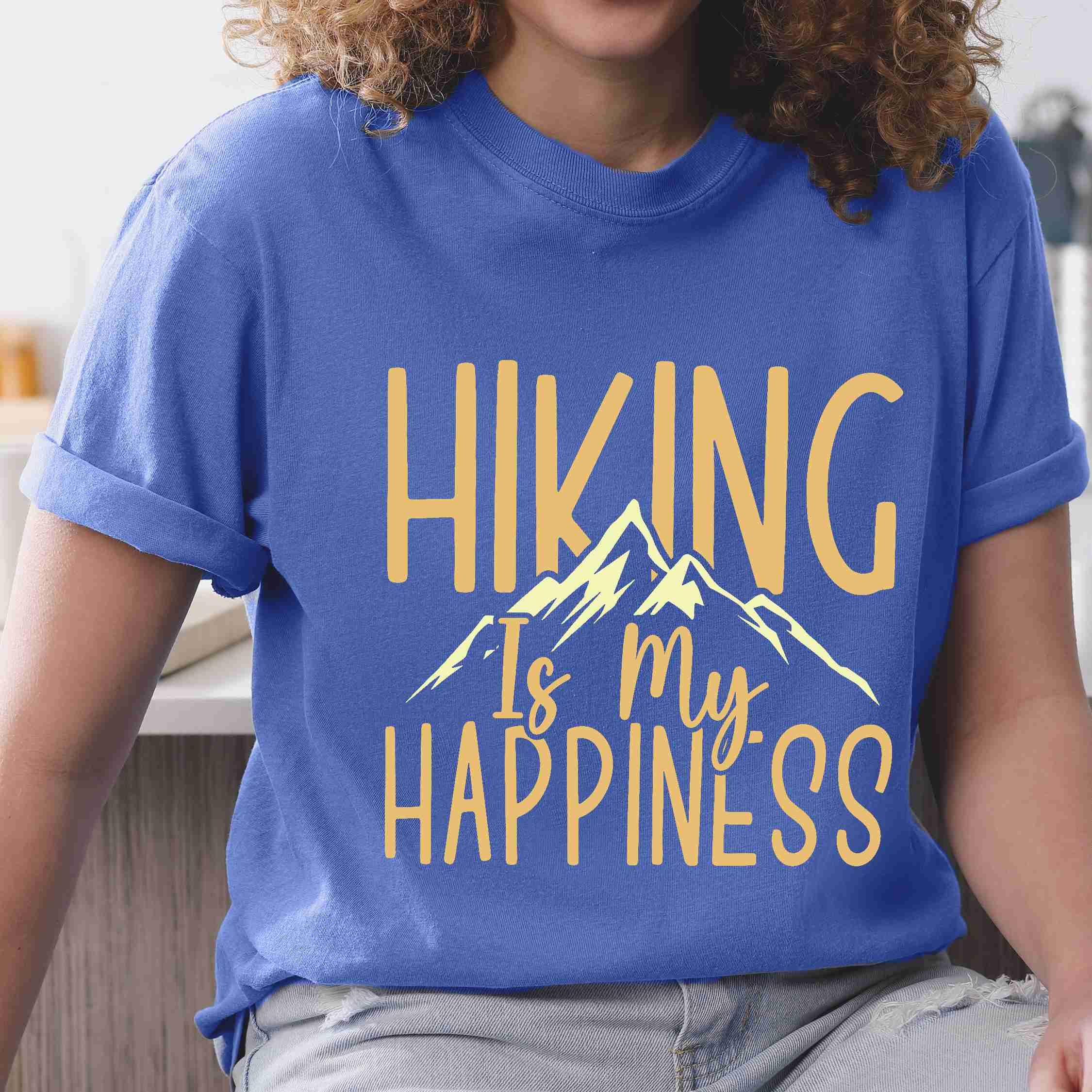 Woman wearing flo blue "hiking is my happiness" colored statement tee with bold typography, mountain, sunrise, perfect for adventure motivated individuals.