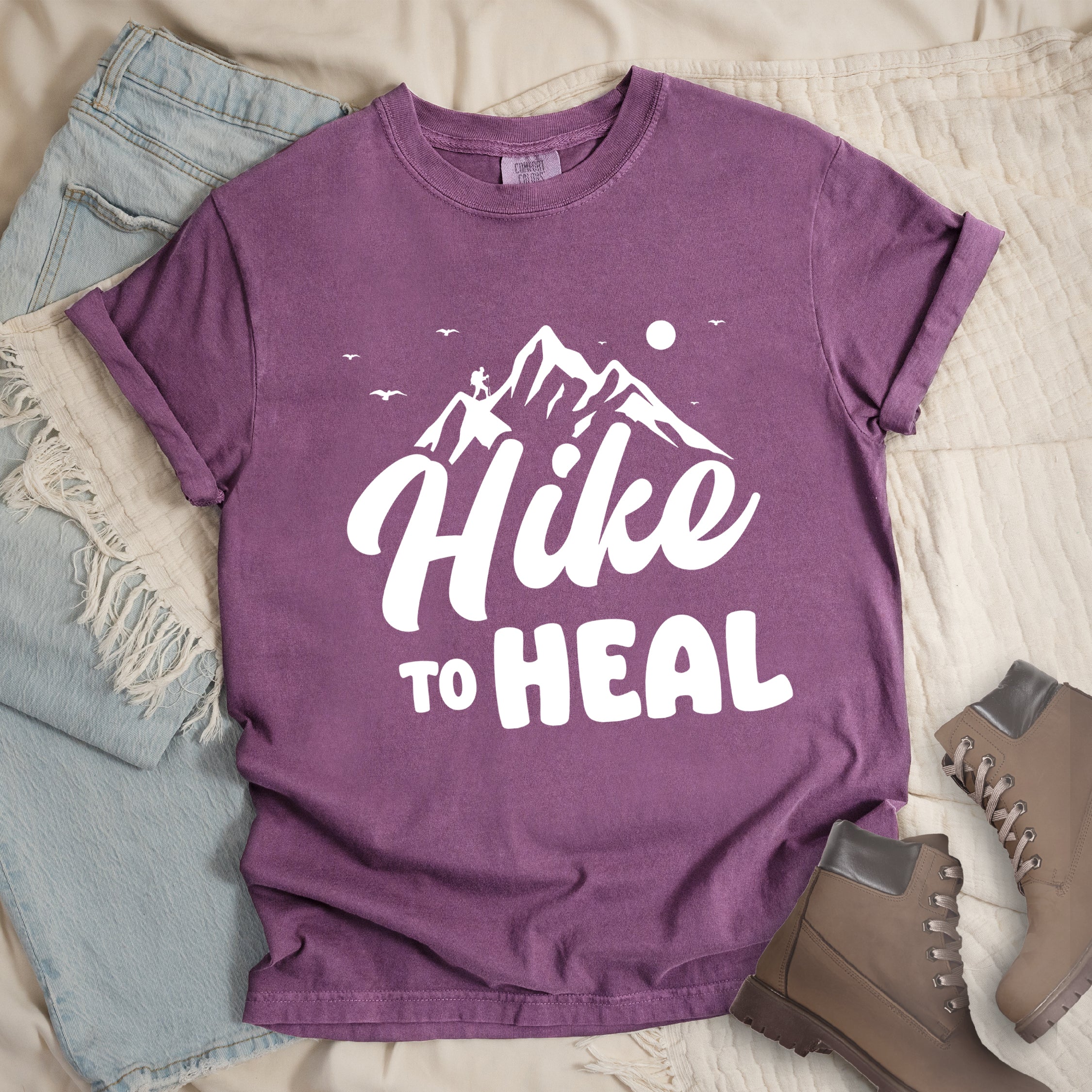 Berry (Dark Violet) graphic t-shirt with 'Hike to Heal' text in white with mountain and bird design, styled with light wash jeans and brown hiking boots