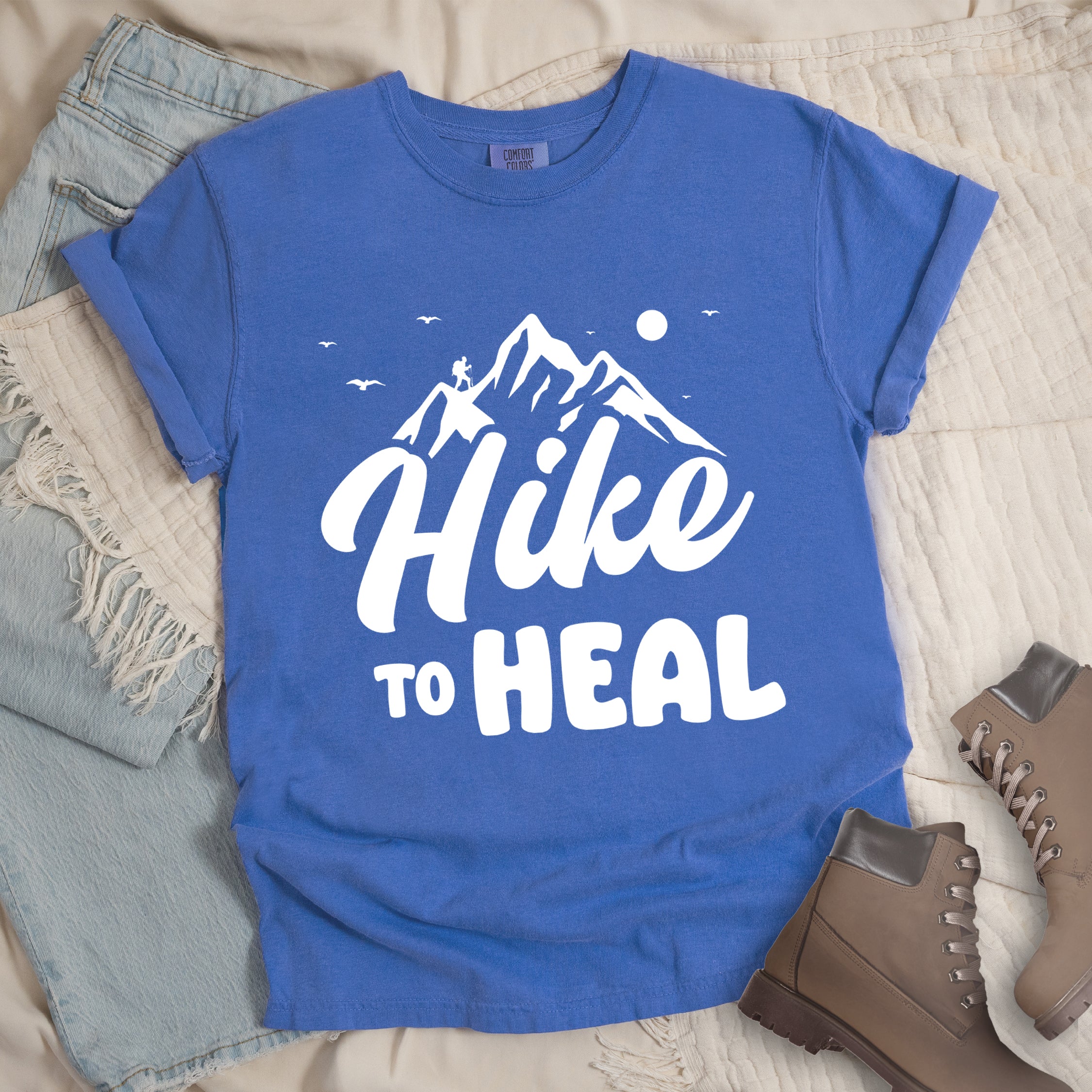 Flo Blue (Bright Blue) graphic t-shirt with 'Hike to Heal' text in white with mountain and bird design, styled with light wash jeans and brown hiking boots