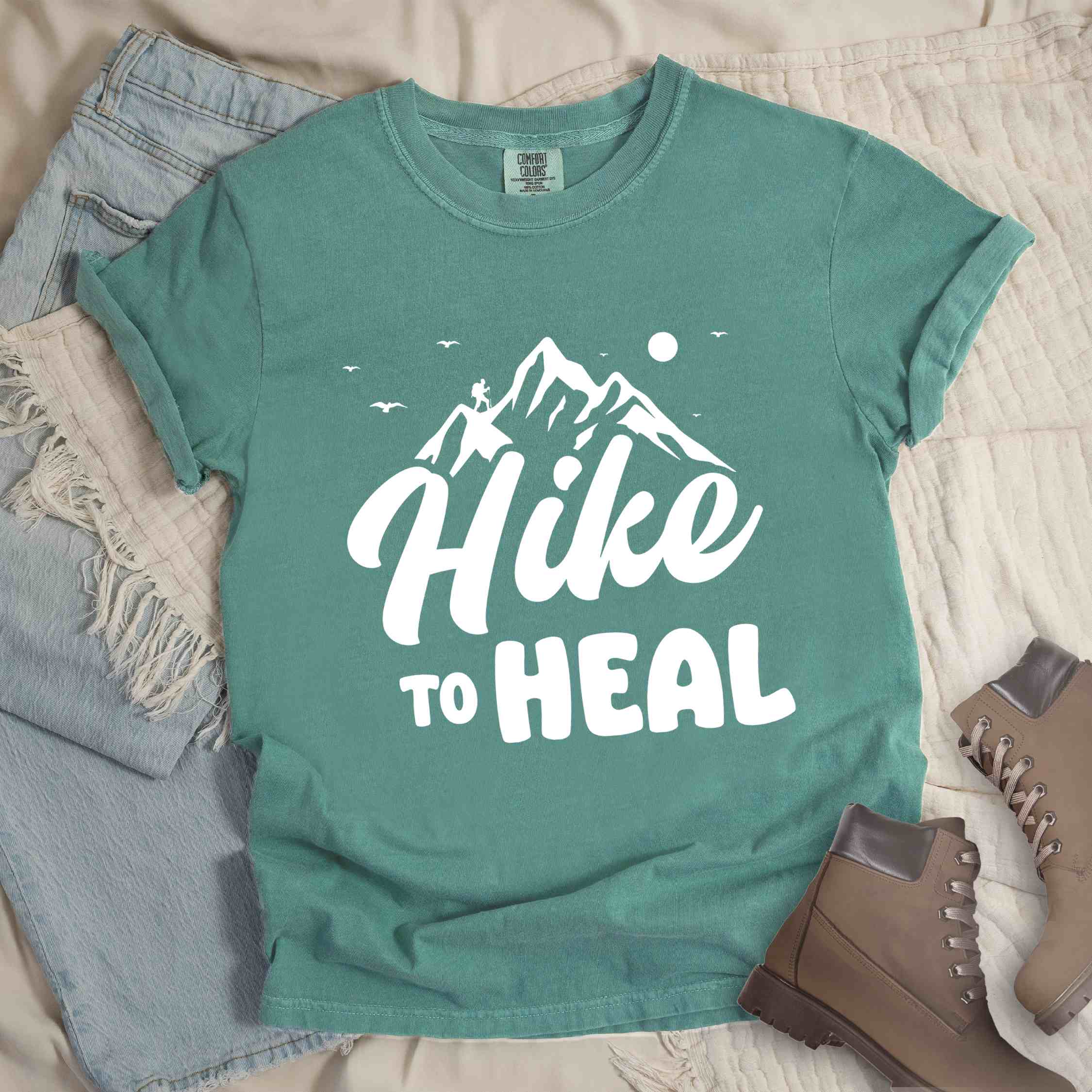 Light green "Hike to Heal" colored statement tee with bold typography, mountain, sunrise, perfect for adventure driven individuals.