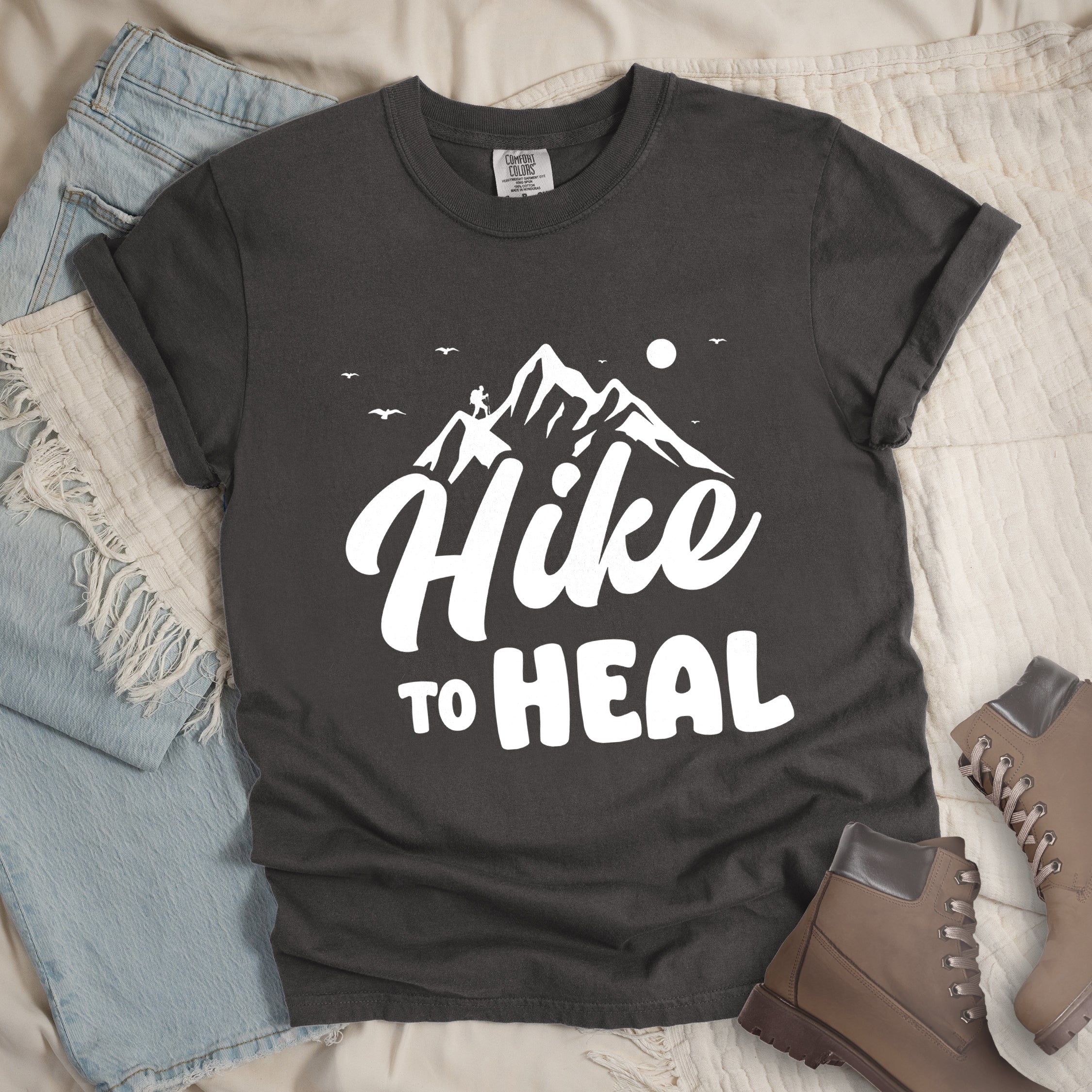 Pepper (Dark Gray) graphic t-shirt with 'Hike to Heal' text in white with mountain and bird design, styled with light wash jeans and brown hiking boots