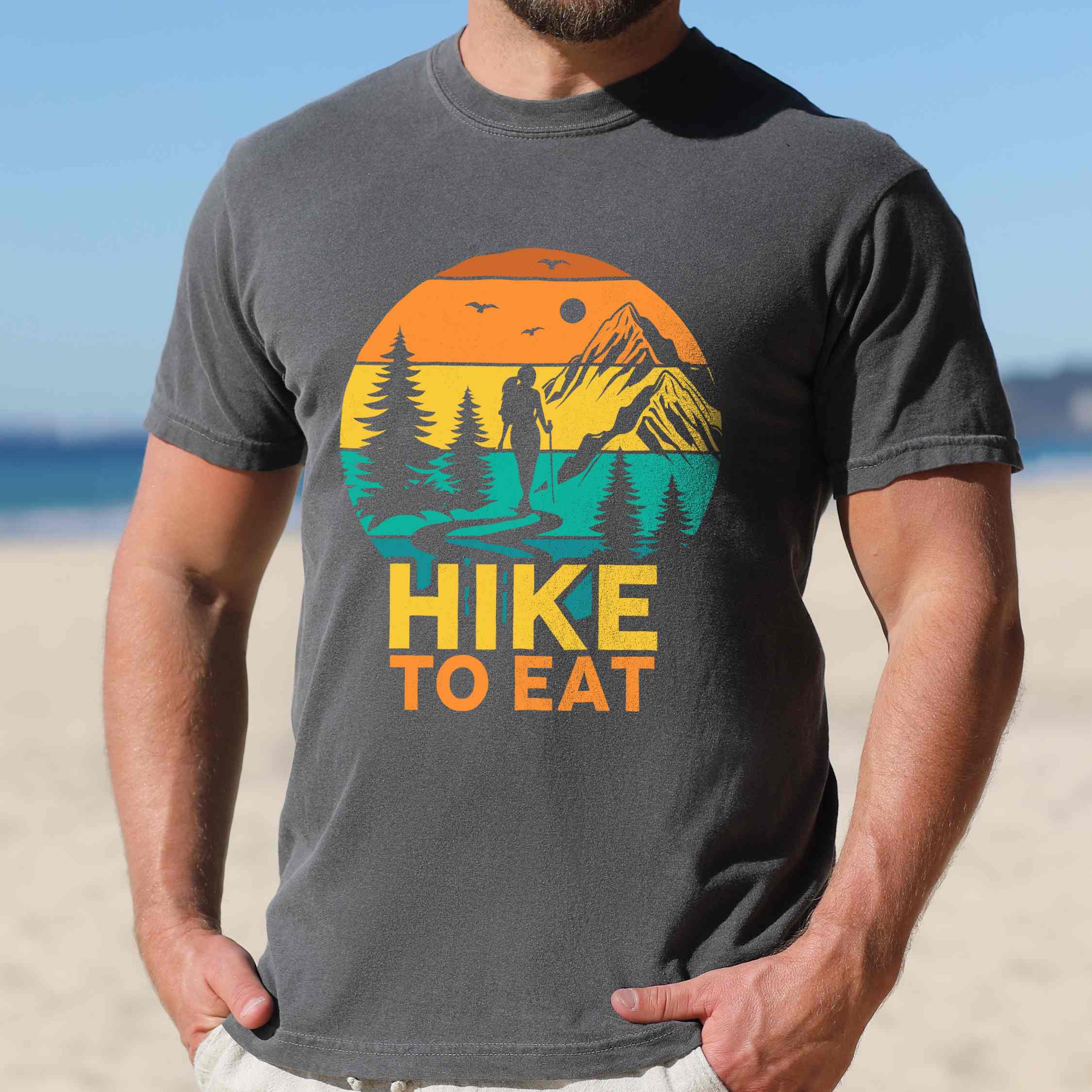 Man wearing pepper "Hike to Eat" colored statement tee with bold typography, mountain, sunrise, perfect for adventure driven individuals.