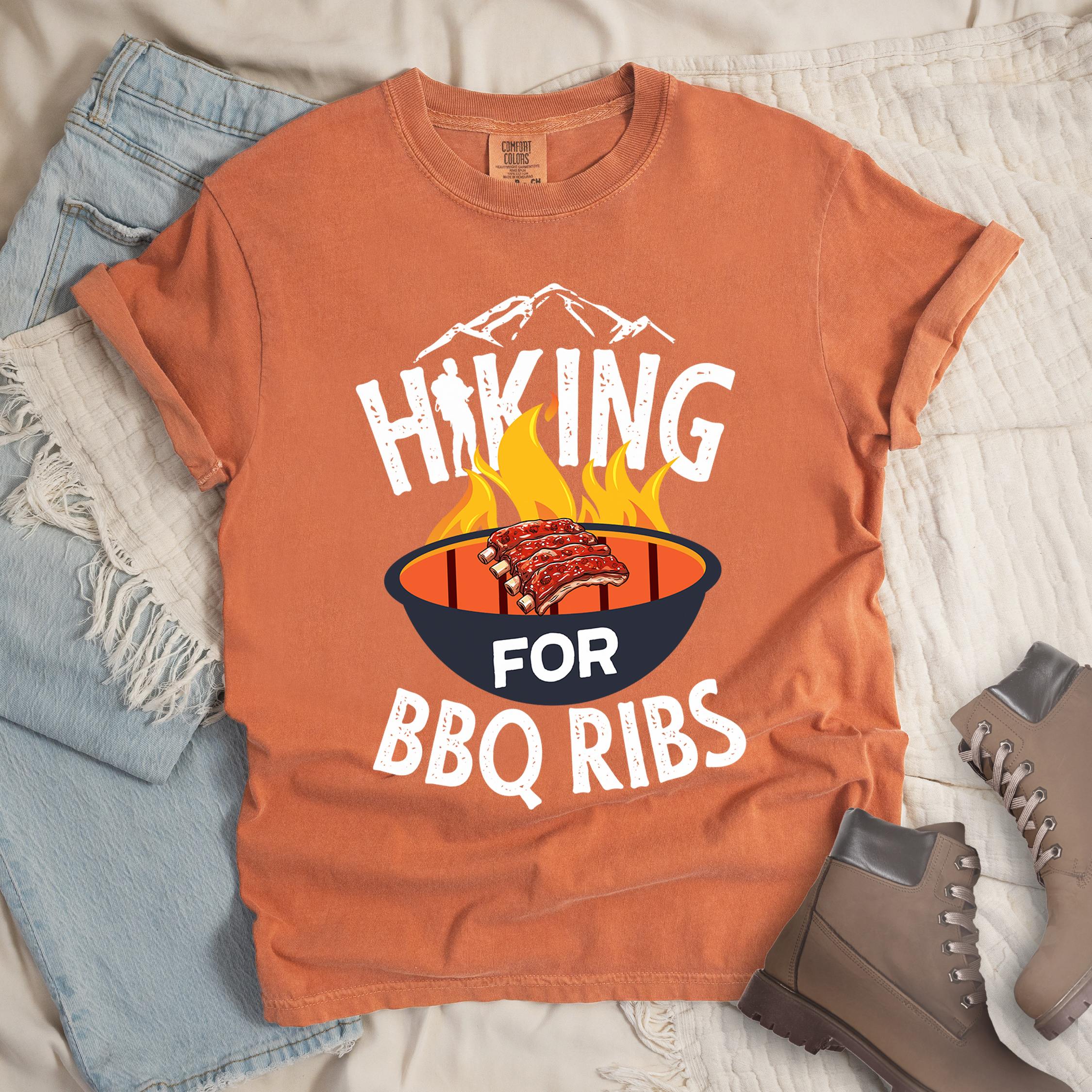 Orange shirt showing a hiking design with 'HIKING FOR BBQ RIBS' phrase and an illustration of BBQ ribs over a fired up grill
