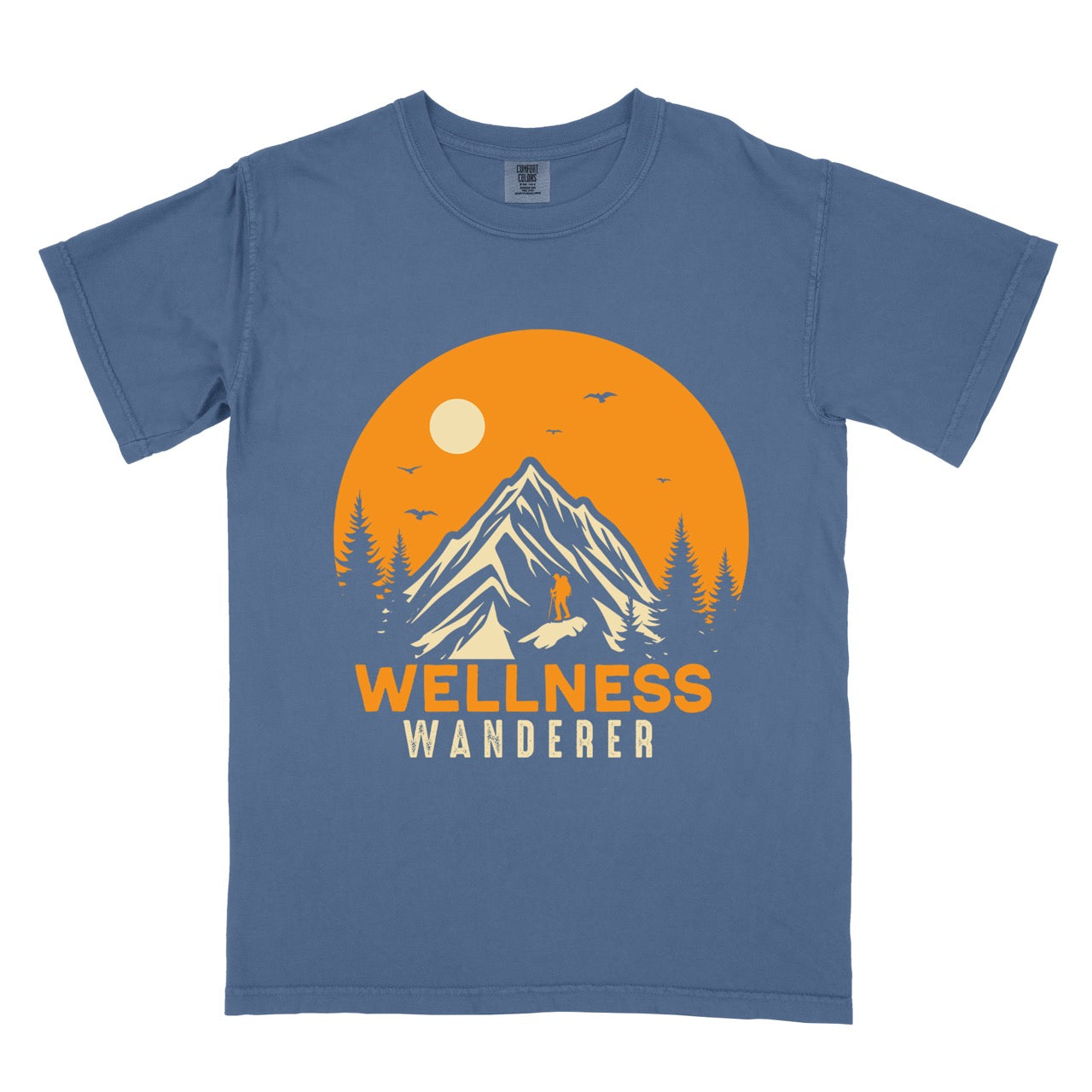 Blue Jean (blue) Wellness lifestyle vintage tee featuring mountain peak landscape with character silhouette at summit orange sunset circle flying birds pine trees and bold Wellness Wanderer typography on Comfort Colors shirt for nature lovers seeking balance