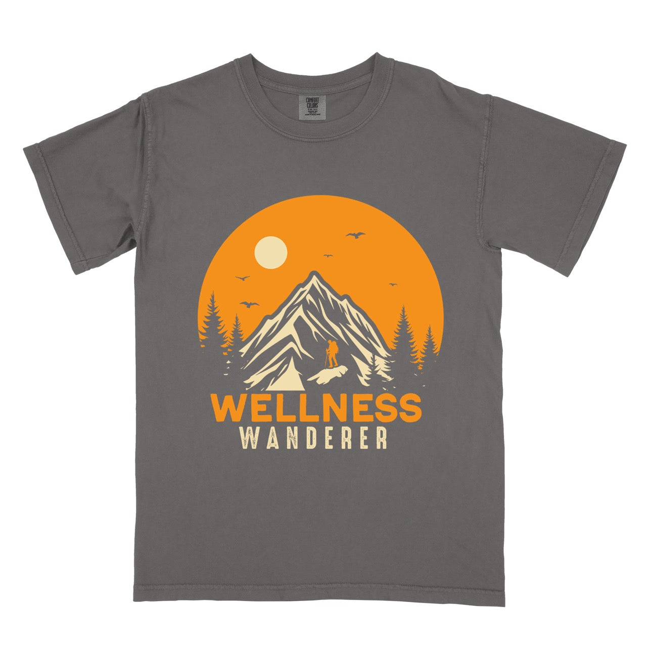 Pepper (grey) Wellness lifestyle vintage tee featuring mountain peak landscape with character silhouette at summit orange sunset circle flying birds pine trees and bold Wellness Wanderer typography on Comfort Colors shirt for nature lovers seeking balance