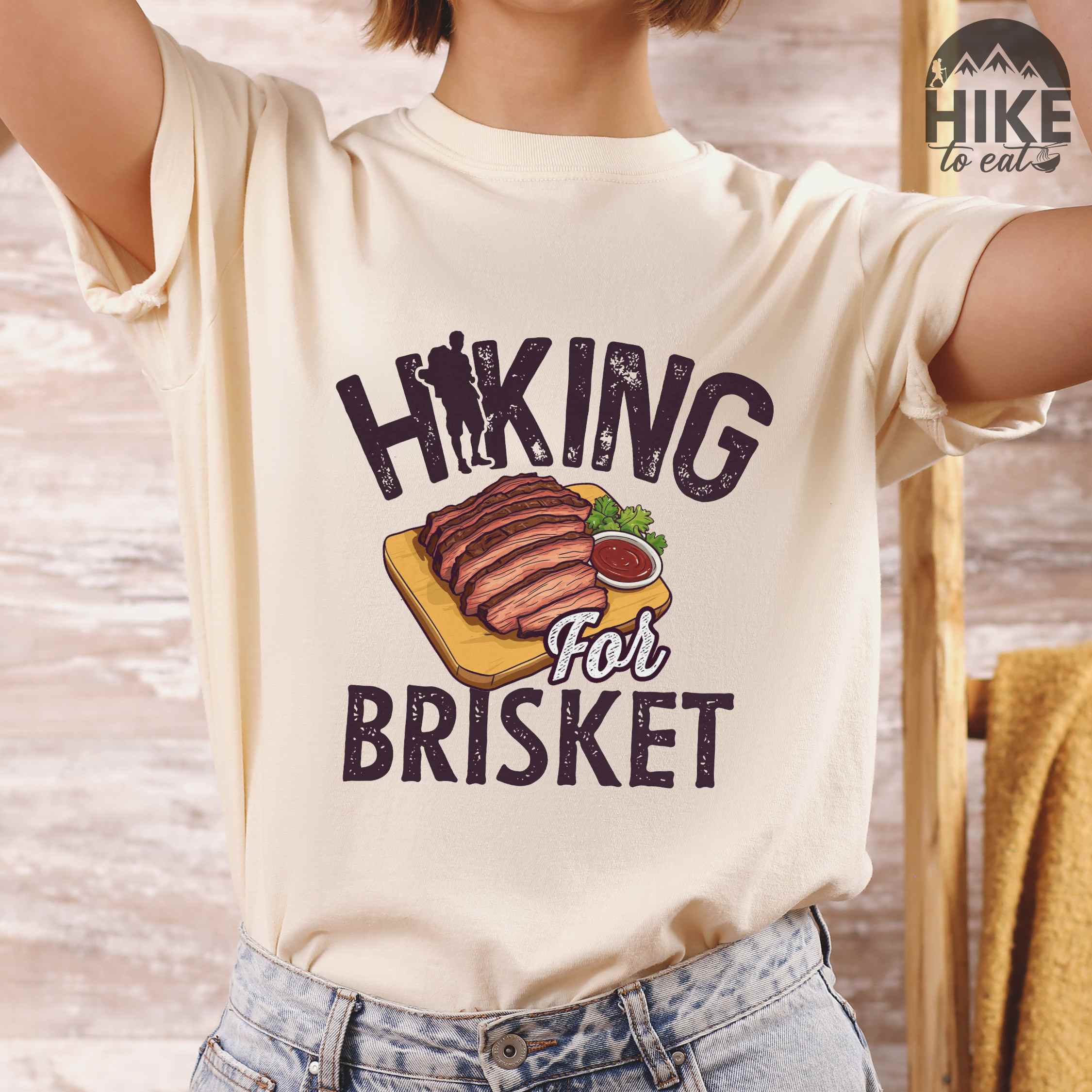 woman wearing ivory Hiking for brisket colored vintage tee with bold typography, illustrated sliced brisket, birds, and backpacker for brisket lovers