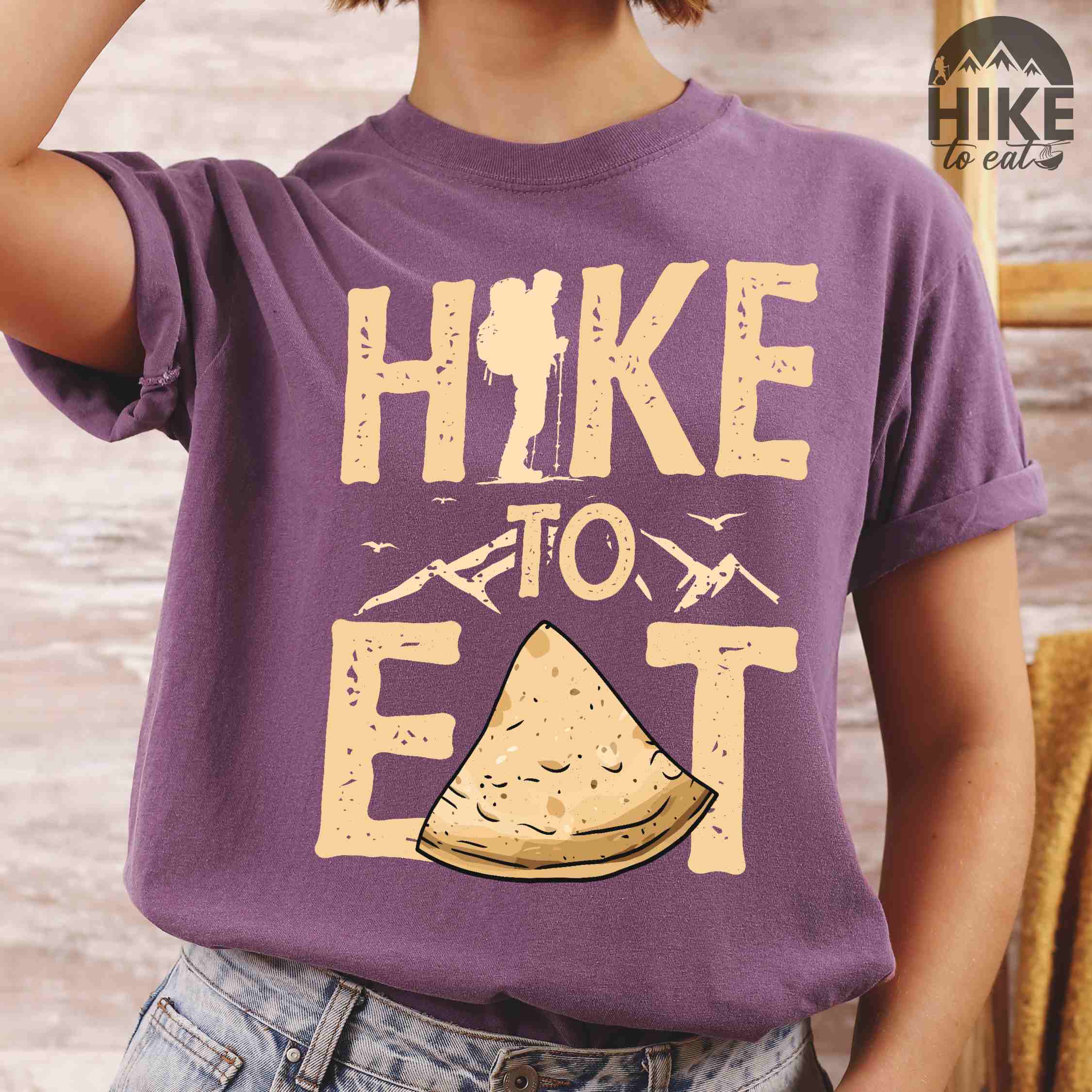 woman wearing berry "Hike to Eat" colored statement tee with bold typography, mountain, illustrated tortilla, perfect for tortilla lovers.