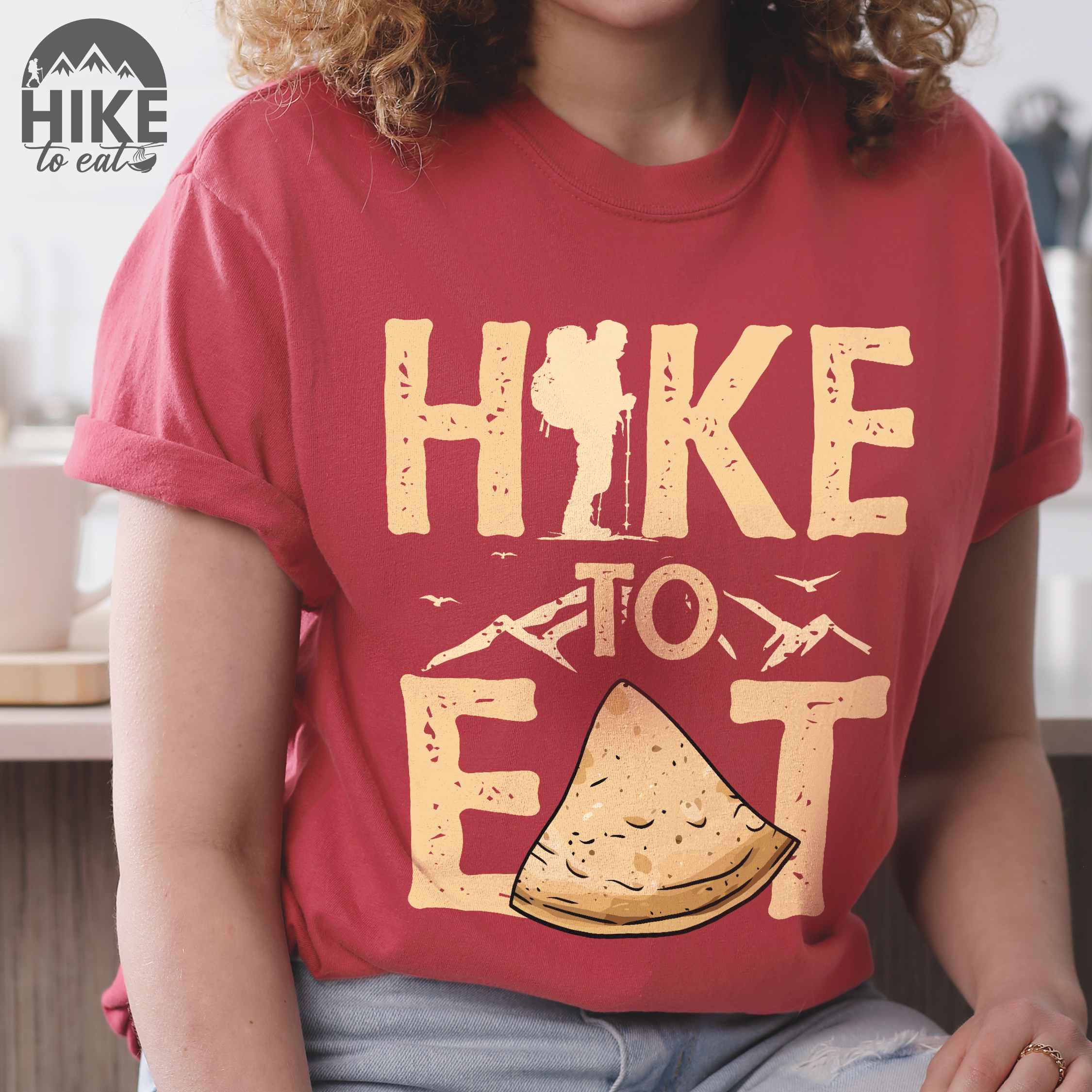 woman wearing crimson "Hike to Eat" colored statement tee with bold typography, mountain, illustrated tortilla, perfect for tortilla lovers.
