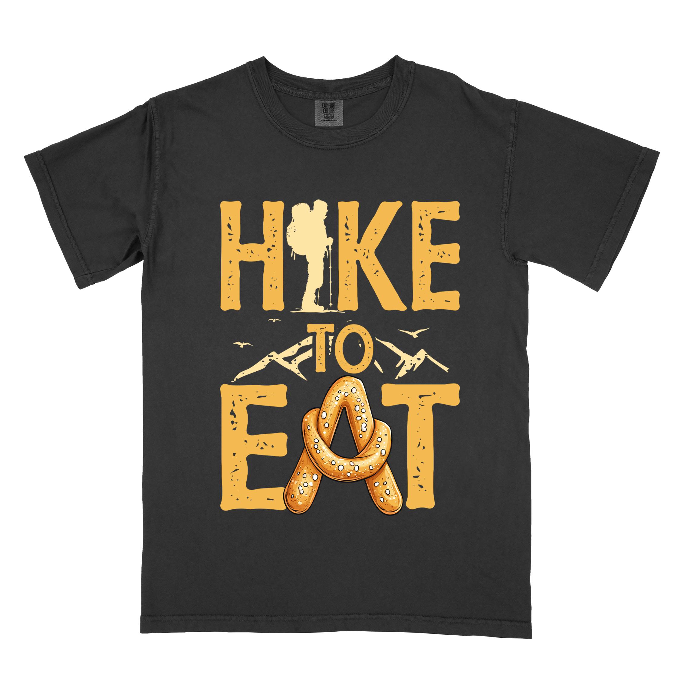 black "Hike to Eat" colored statement tee with bold typography, mountain, illustrated baked pretzel, and backpacker for pastry enthusiasts.