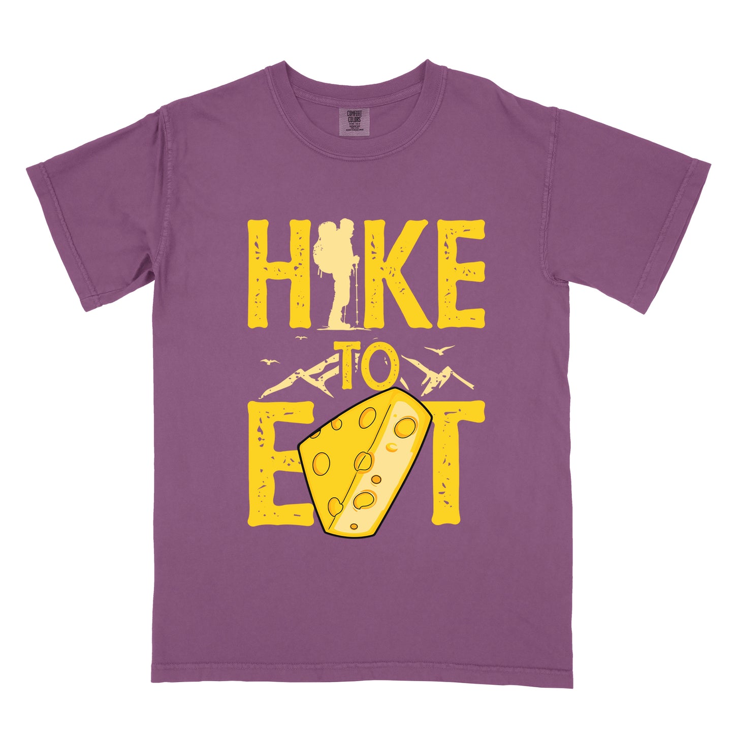 Berry (Dark Violet) t-shirt with yellow distressed text reading "HIKE TO EAT". "HIKE" appears in large yellow letters at the top with a hiker silhouette integrated into the letter "I", "TO" in yellow text with mountain outlines on either side in the middle, and "EAT" in large yellow letters at the bottom with a wedge of Swiss cheese positioned between "E" and "T". Small flying birds appear near "TO". The design connects hiking with eating cheese as motivation.
