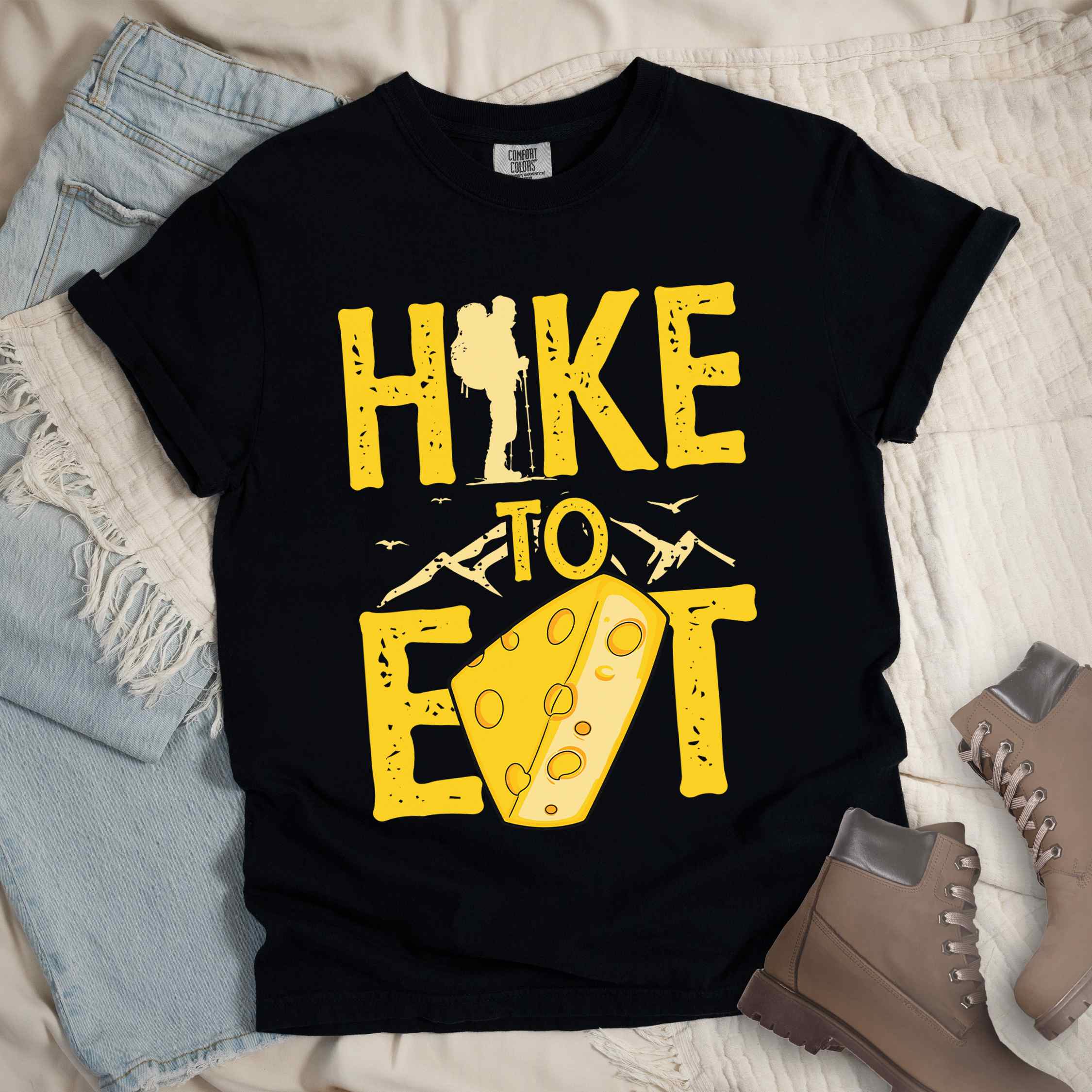 black "Hike to Eat" colored statement tee with bold typography, mountain, illustrated slice of cheese, and backpacker for cheese lovers.