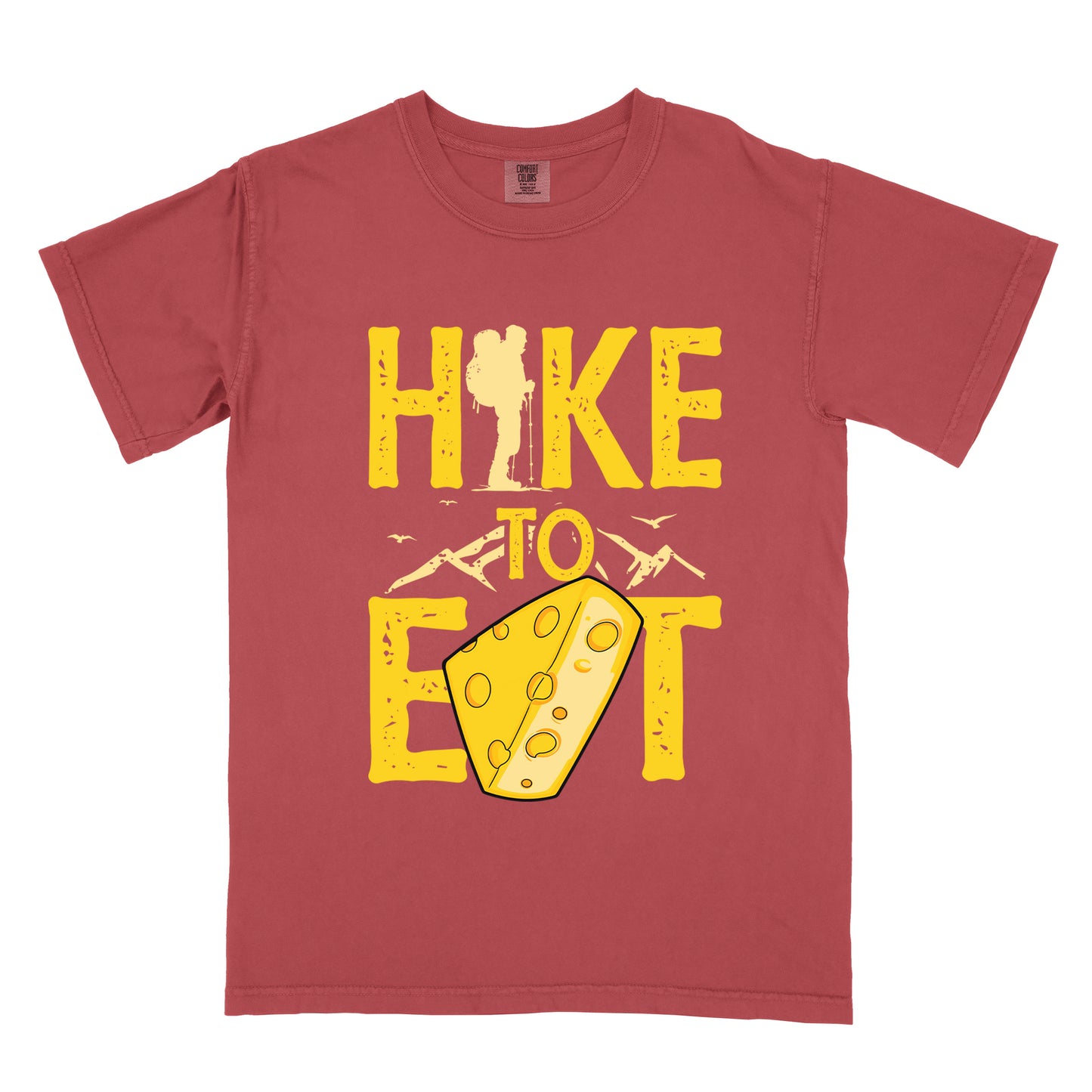 Crimson (Dark Pink) t-shirt with yellow distressed text reading "HIKE TO EAT". "HIKE" appears in large yellow letters at the top with a hiker silhouette integrated into the letter "I", "TO" in yellow text with mountain outlines on either side in the middle, and "EAT" in large yellow letters at the bottom with a wedge of Swiss cheese positioned between "E" and "T". Small flying birds appear near "TO". The design connects hiking with eating cheese as motivation.