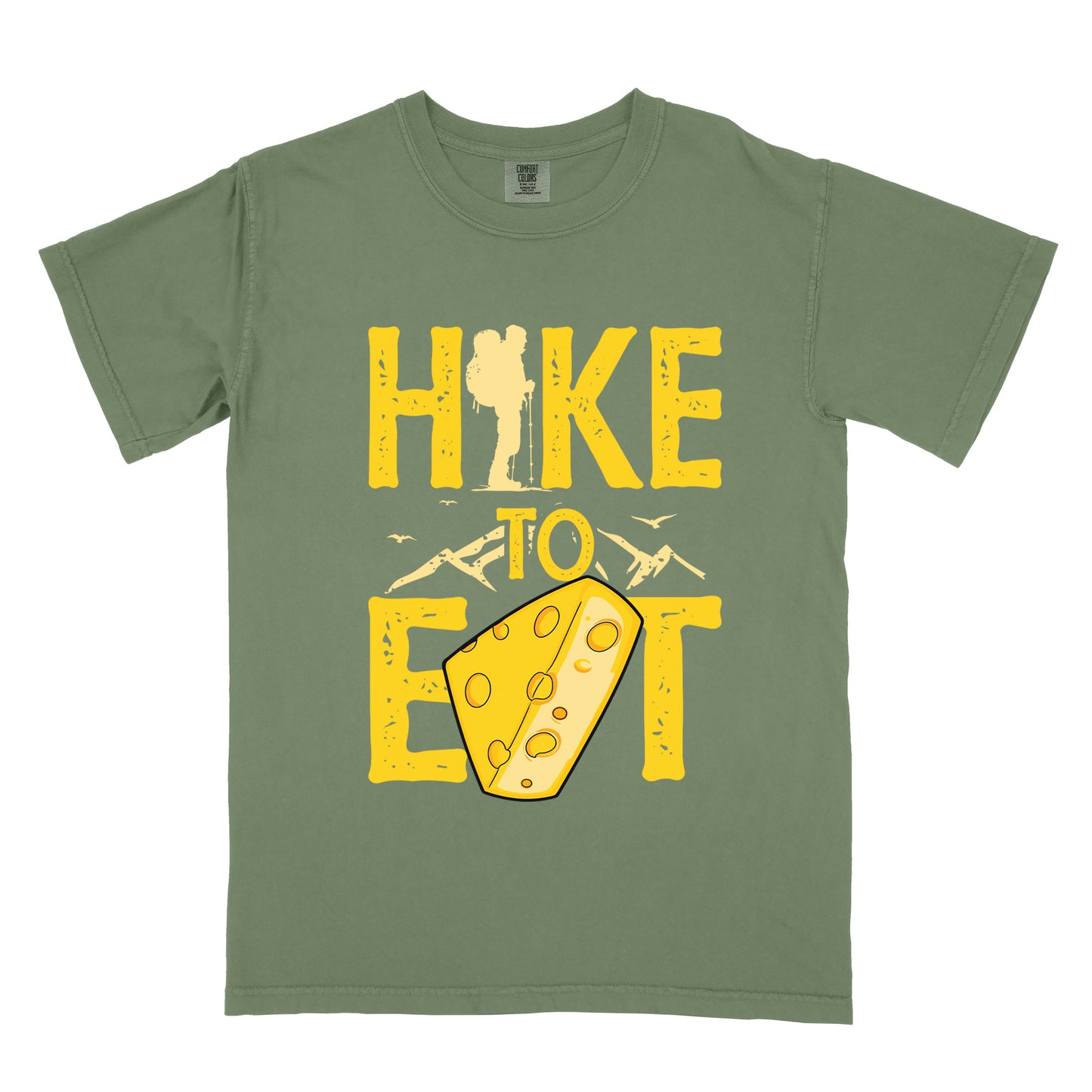 Moss (Dark Green) t-shirt with yellow distressed text reading "HIKE TO EAT". "HIKE" appears in large yellow letters at the top with a hiker silhouette integrated into the letter "I", "TO" in yellow text with mountain outlines on either side in the middle, and "EAT" in large yellow letters at the bottom with a wedge of Swiss cheese positioned between "E" and "T". Small flying birds appear near "TO". The design connects hiking with eating cheese as motivation.