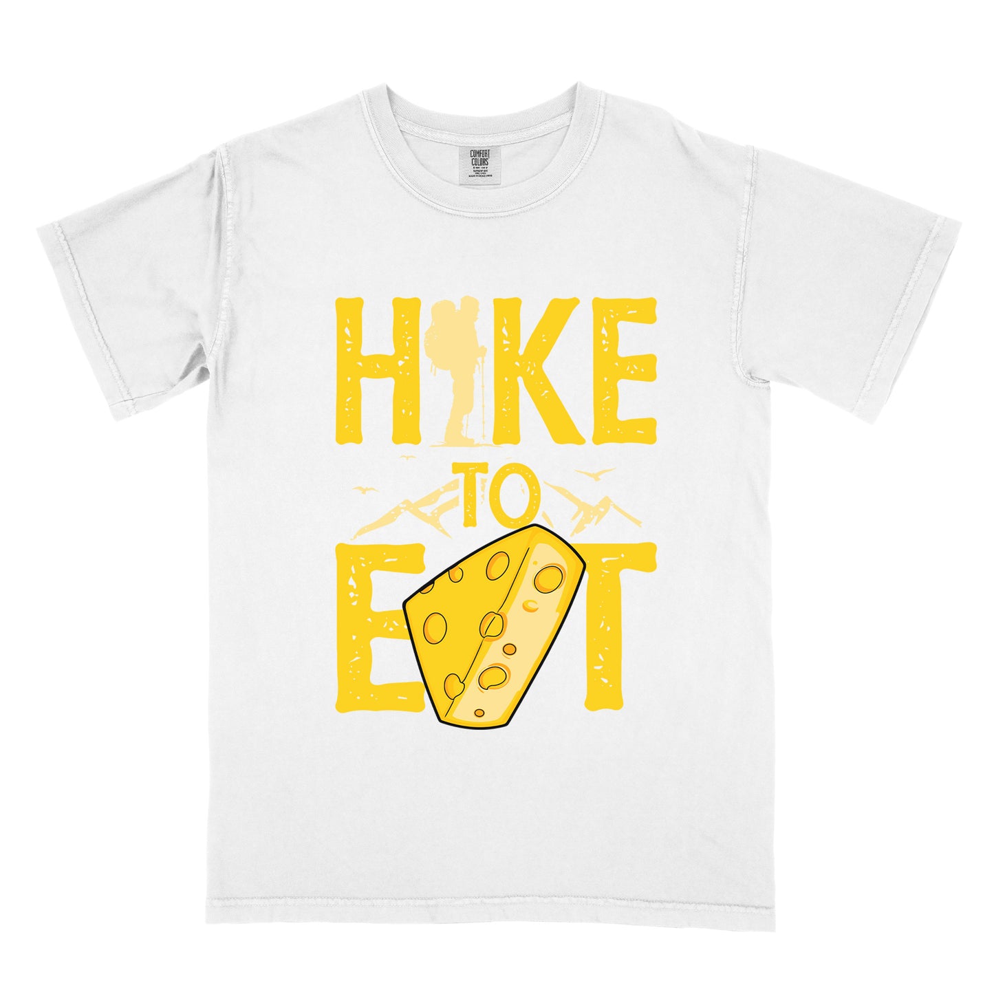 White t-shirt with yellow distressed text reading "HIKE TO EAT". "HIKE" appears in large yellow letters at the top with a hiker silhouette integrated into the letter "I", "TO" in yellow text with mountain outlines on either side in the middle, and "EAT" in large yellow letters at the bottom with a wedge of Swiss cheese positioned between "E" and "T". Small flying birds appear near "TO". The design connects hiking with eating cheese as motivation.