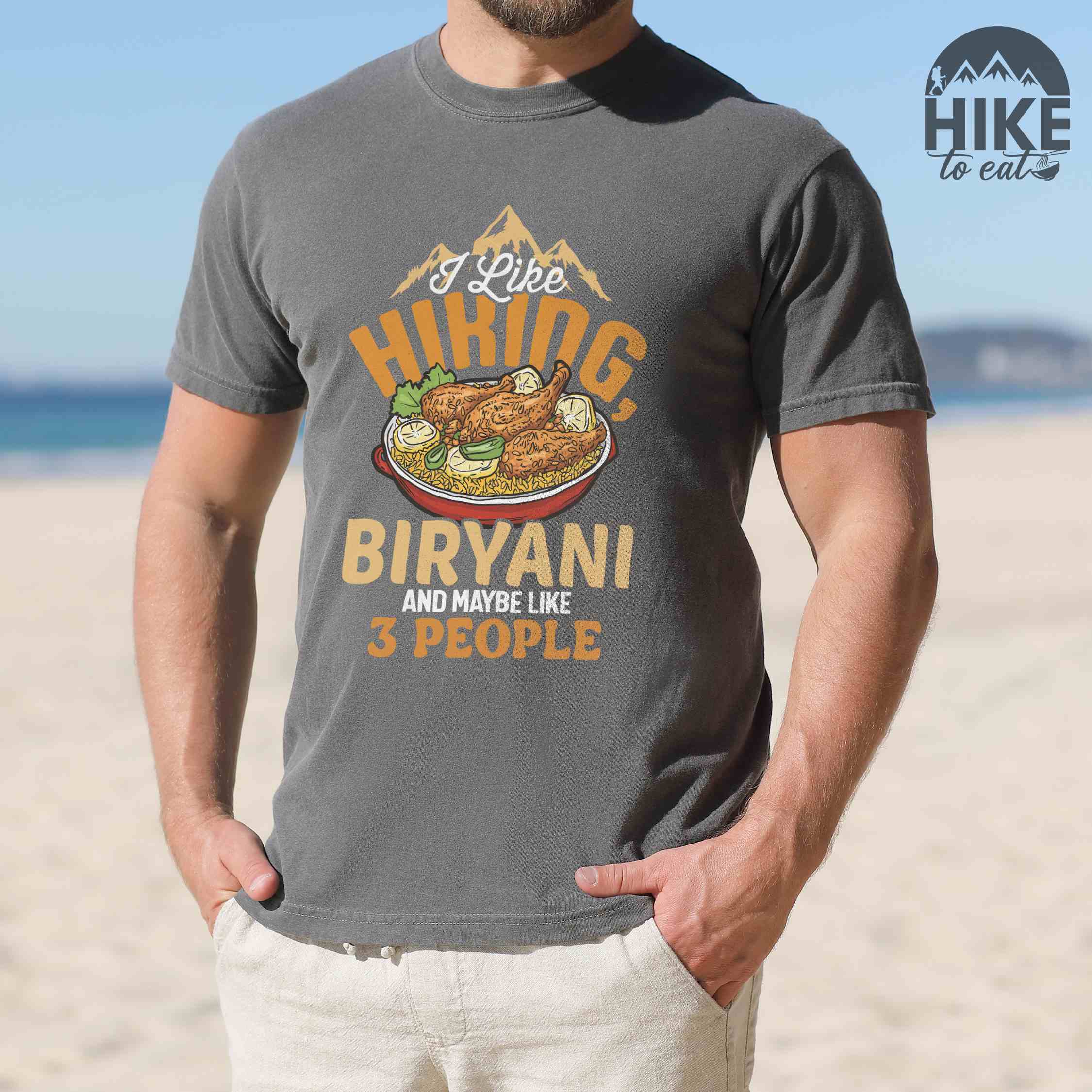 Man wearing pepper “I Like Hiking, Biryani and Maybe Like 3 People” colored vintage tee with bold text, featuring a steaming bowl of biryani with chicken, lemon wedges, and herbs. Perfect tee for biryani rice lovers.