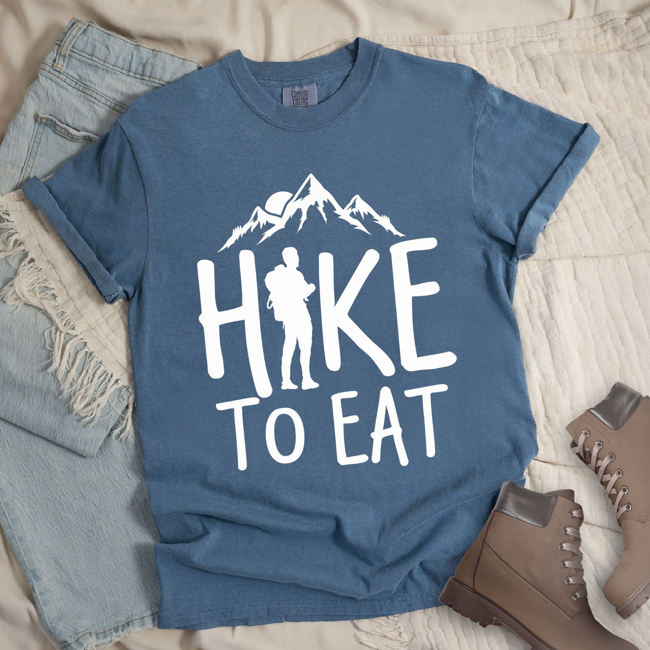Dark blue shirt with a Hiking design featuring mountain silhouette and shows 'Hike To Eat' phrase in bold text