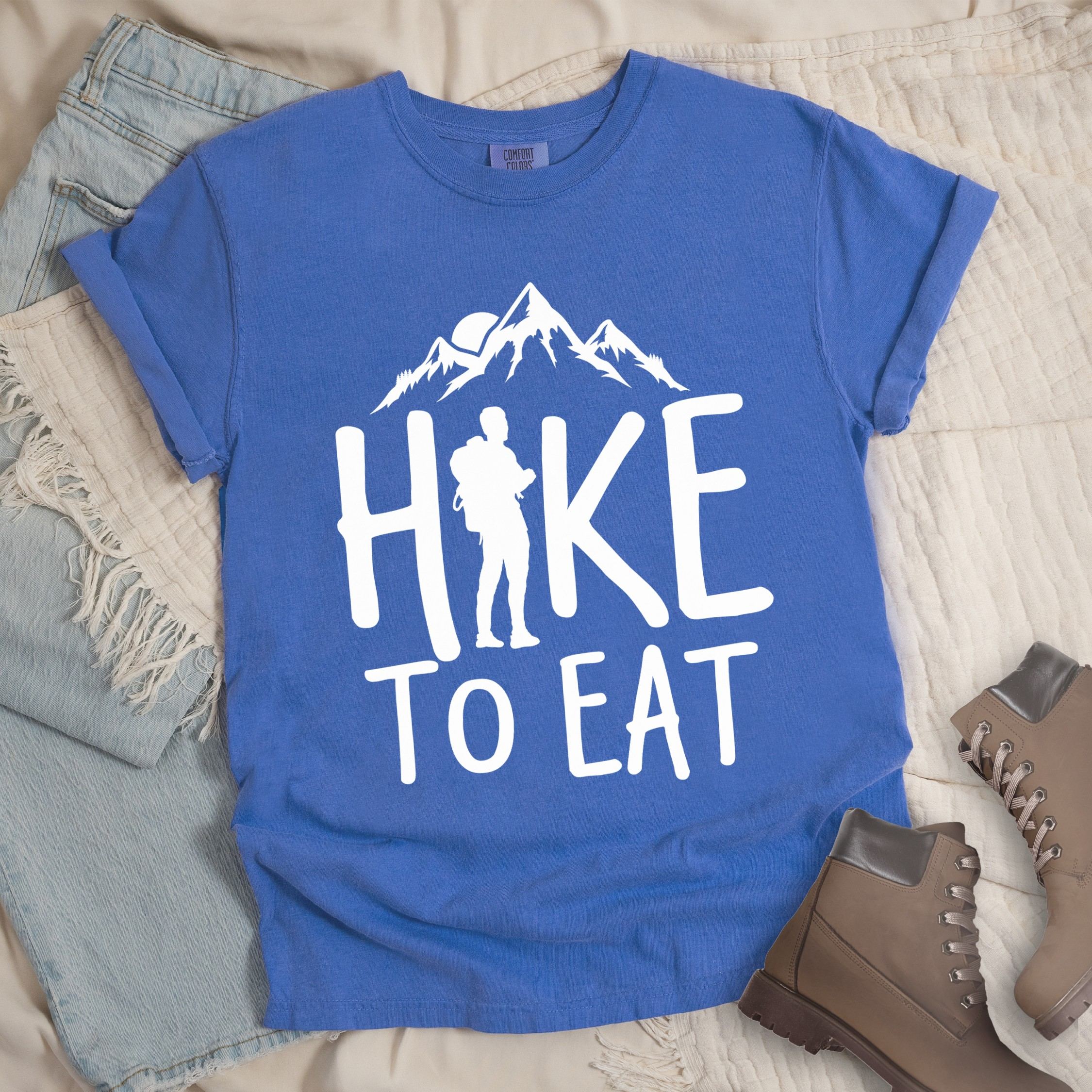 Blue shirt with a Hiking design featuring mountain silhouette and shows 'Hike To Eat' phrase in bold text