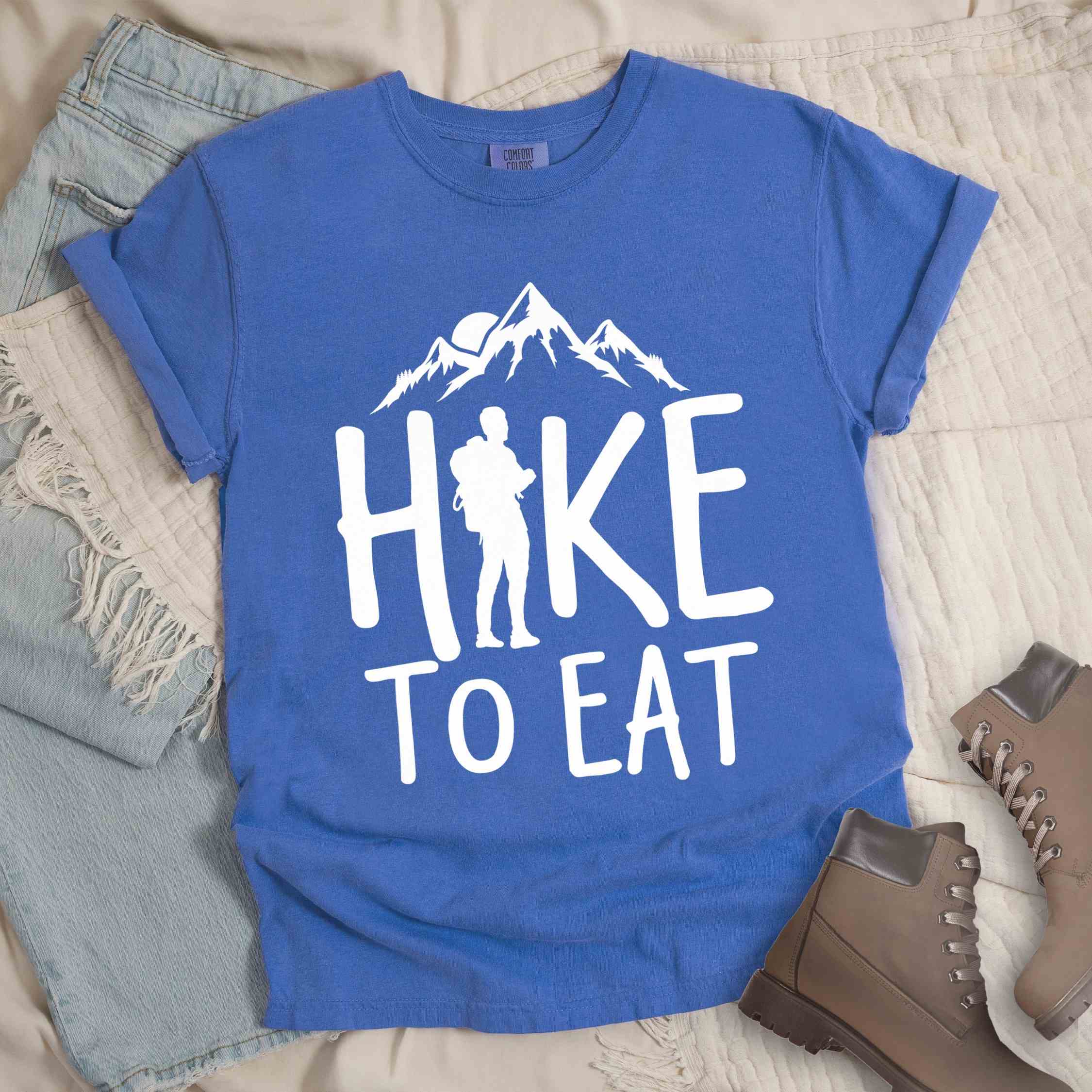 Flo blue "Hike to Eat" colored statement tee with bold typography, mountains, birds, sunrise, perfect for food motivated individuals.