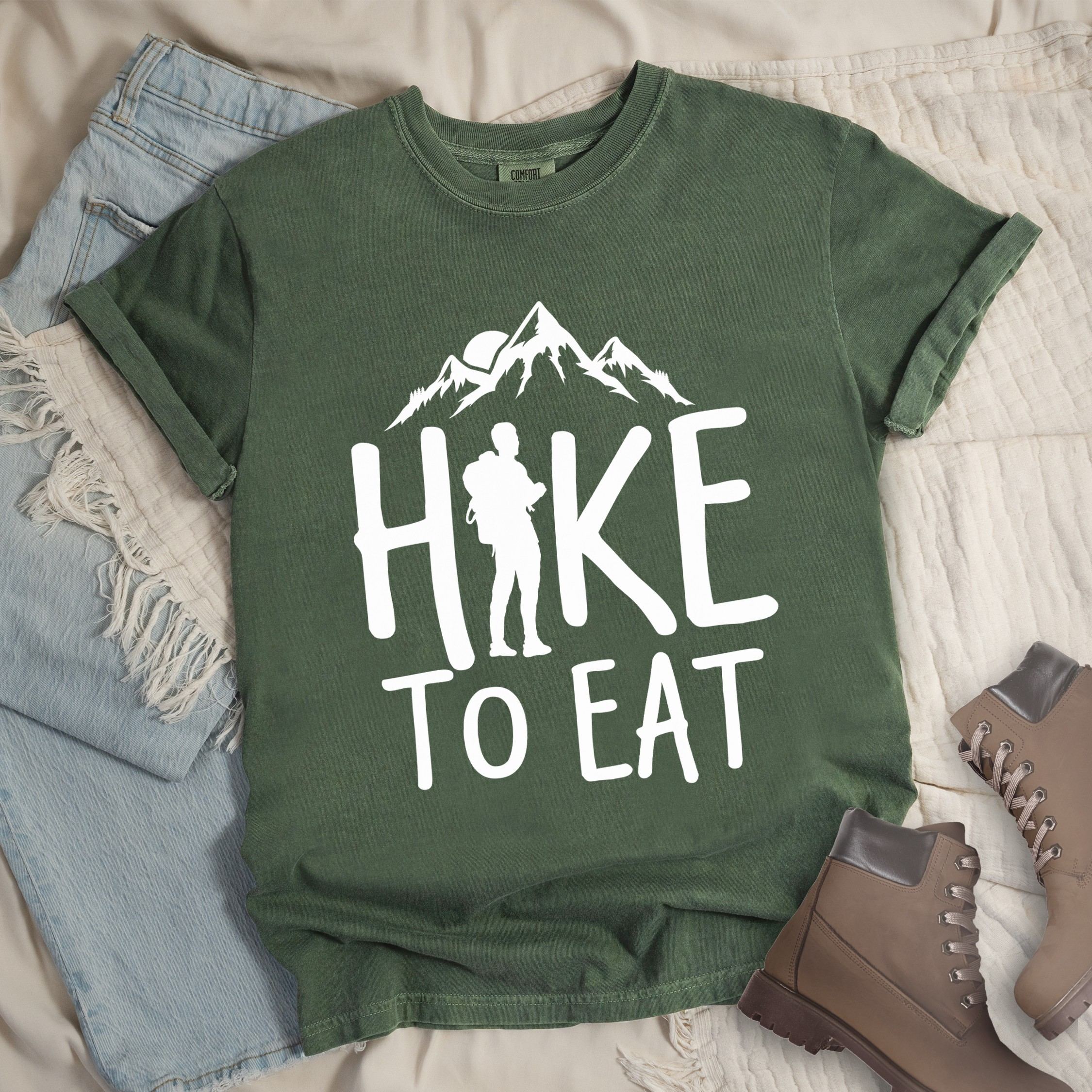 Dark green shirt with a Hiking design featuring mountain silhouette and shows 'Hike To Eat' phrase in bold text