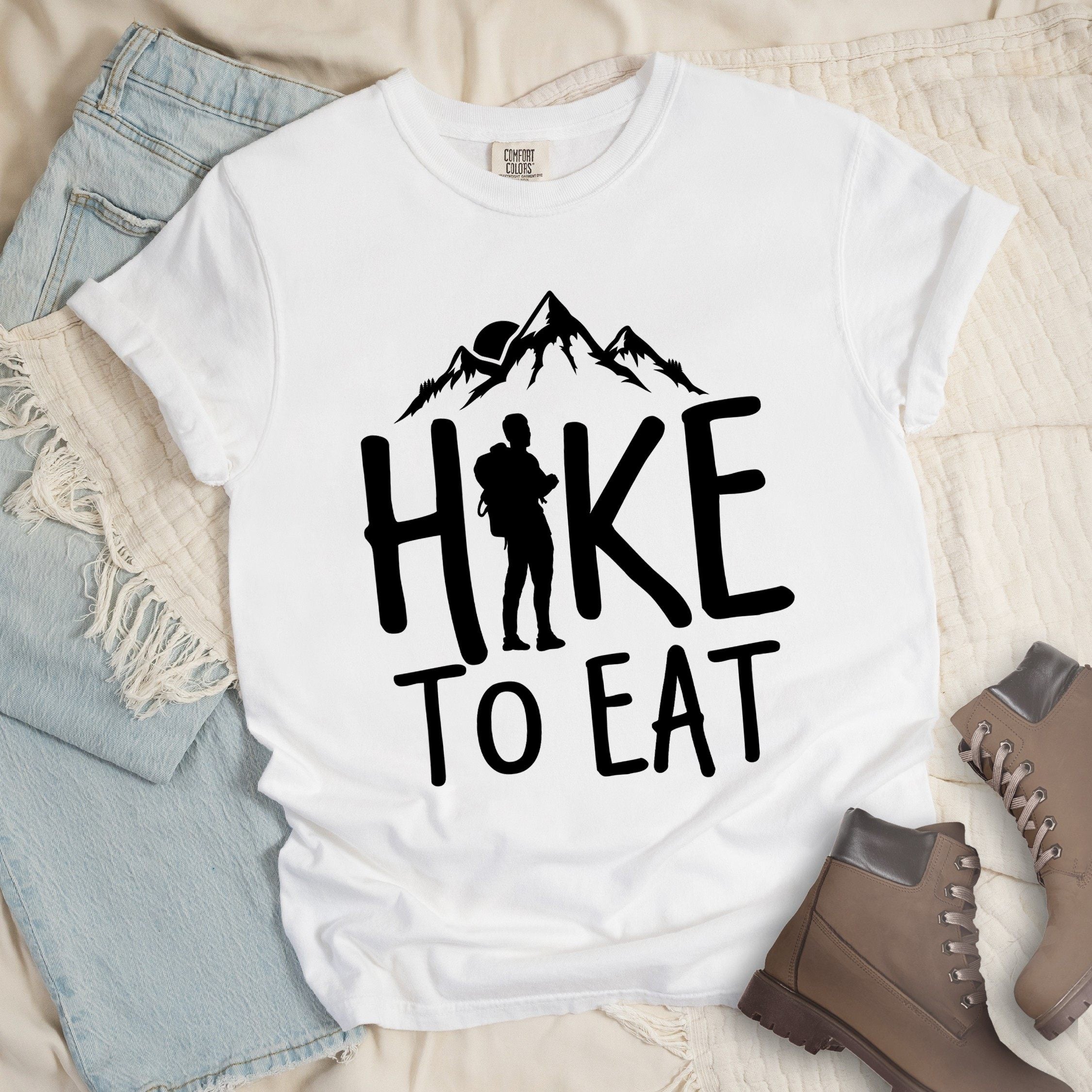 White shirt with a Hiking design featuring mountain silhouette and shows 'Hike To Eat' phrase in bold text