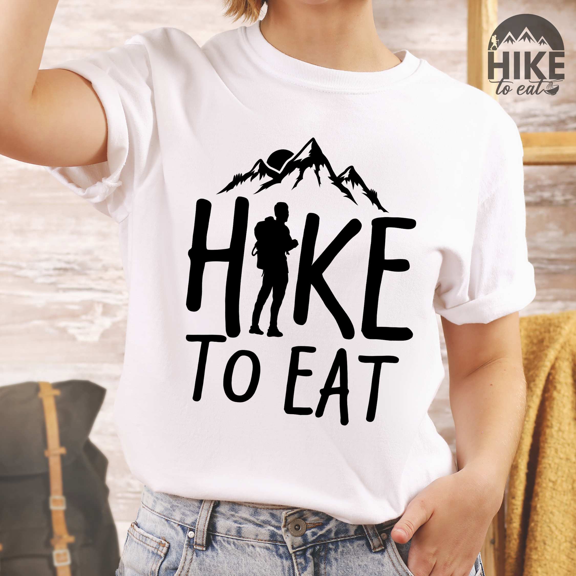 Woman wearing white "Hike to Eat" colored statement tee with bold typography, mountains, birds, sunrise, perfect for food motivated individuals.