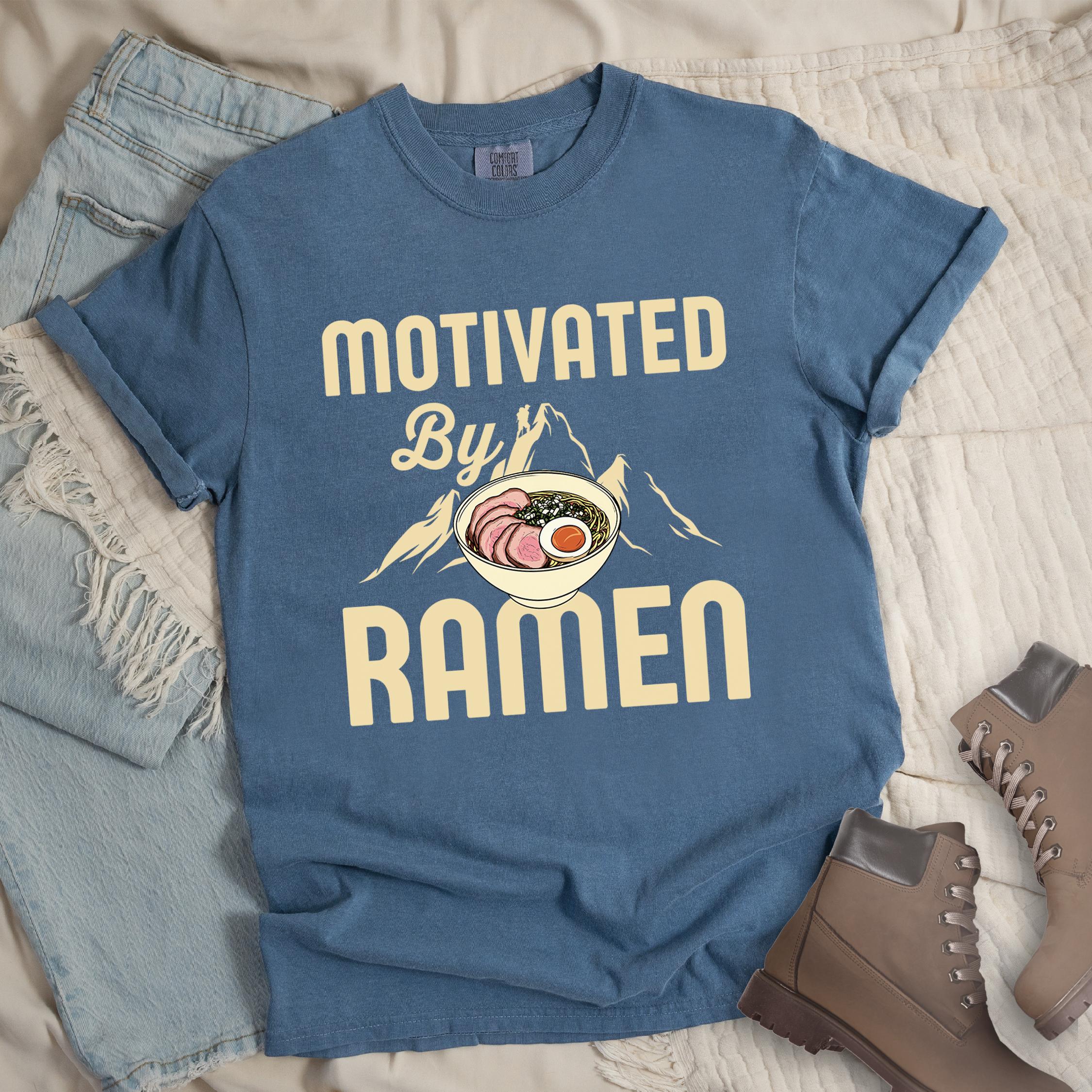 Dark blue shirt with “Motivated by Ramen” in cream-colored text, featuring a ramen bowl with pork, egg, and seaweed in front of mountain peaks.