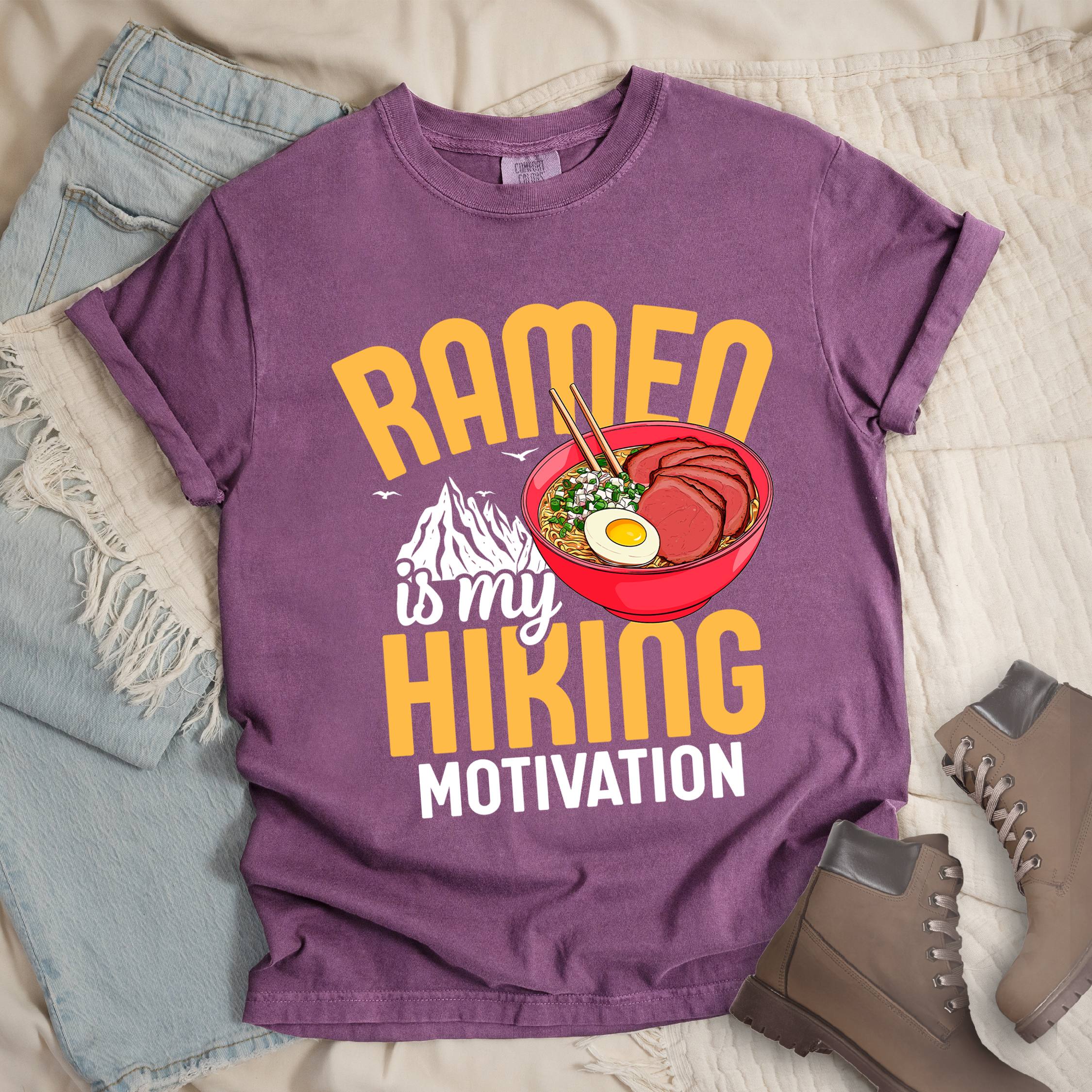 Dark pink shirt with “Ramen is my Hiking Motivation” text, featuring a mountain graphic and a ramen bowl with noodles, egg, meat, and chopsticks.