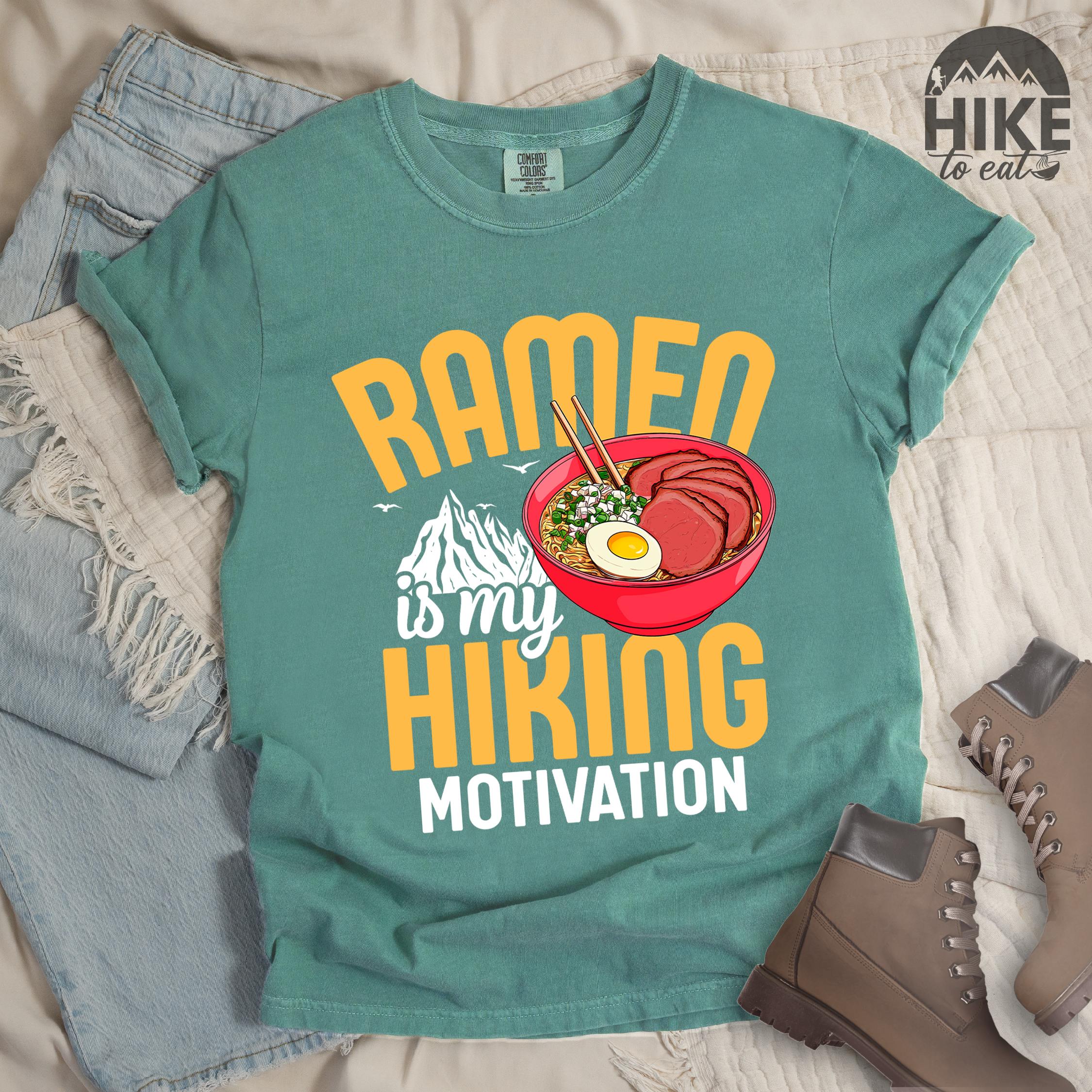 Green shirt with “Ramen is my Hiking Motivation” text, featuring a mountain graphic and a ramen bowl with noodles, egg, meat, and chopsticks.