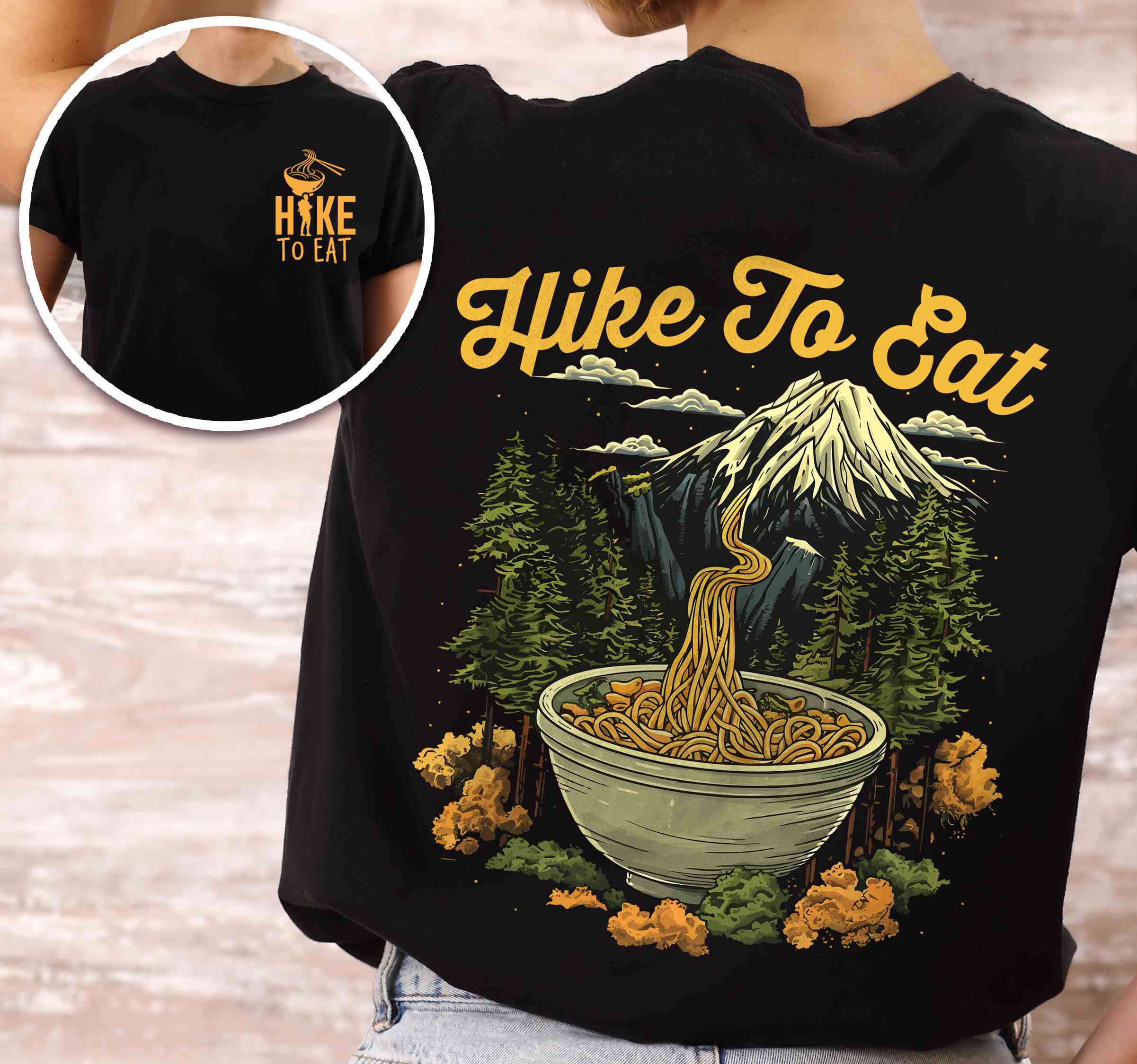 woman wearing black "Hike to Eat" text in cream lettering, mountains, birds, illustrated bowl of ramen noodles, and backpacker for ramen lovers.