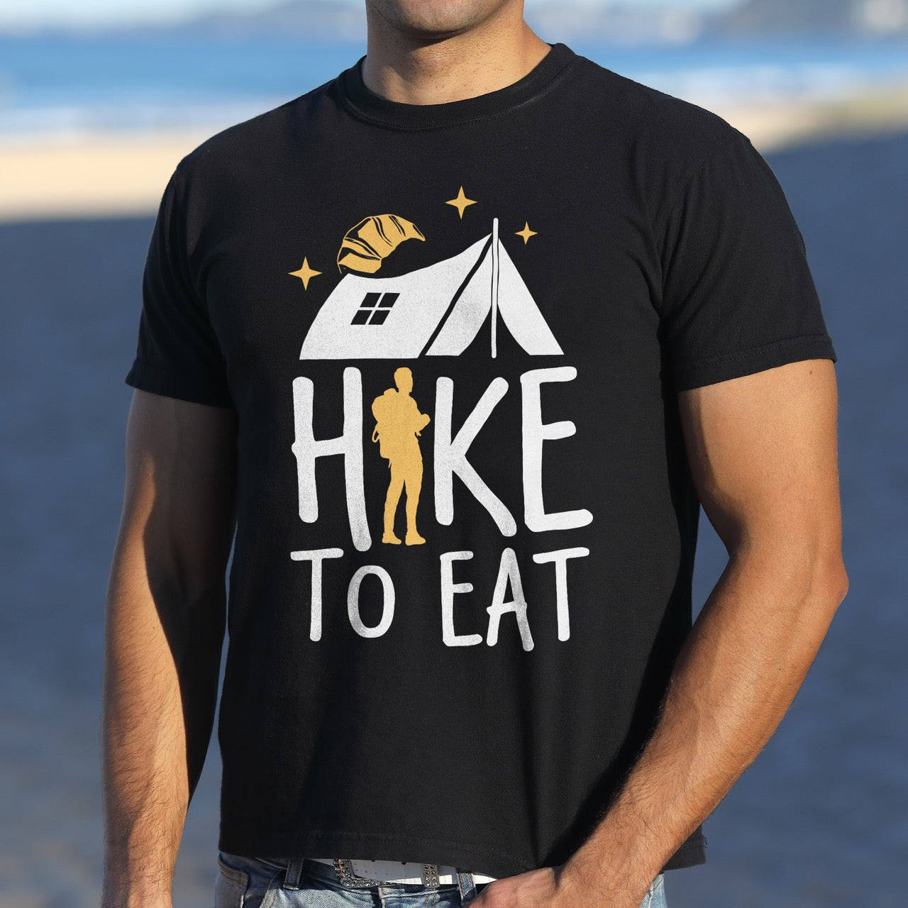 Man wearing Black Hike to Eat brand philosophy vintage tee with white camping tent croissant moon stars character silhouette with backpack integrated into typography on Comfort Colors shirt for food motivated adventurers, outdoor enthusiasts and hikers