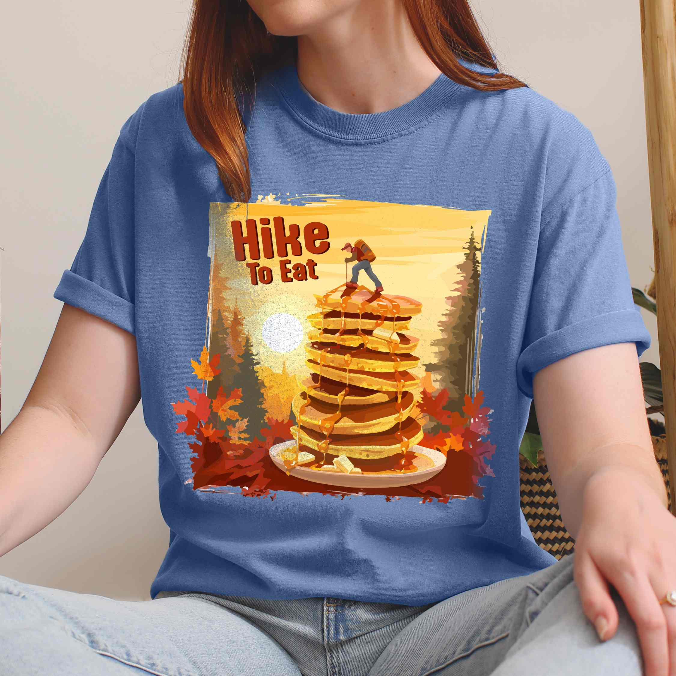 Woman wearing blue jean "Hike to Eat" colored vintage statement tee with text in bold lettering, mountains, birds, silhouette, illustrated stack of pancake, and perfect for breakfast lovers.