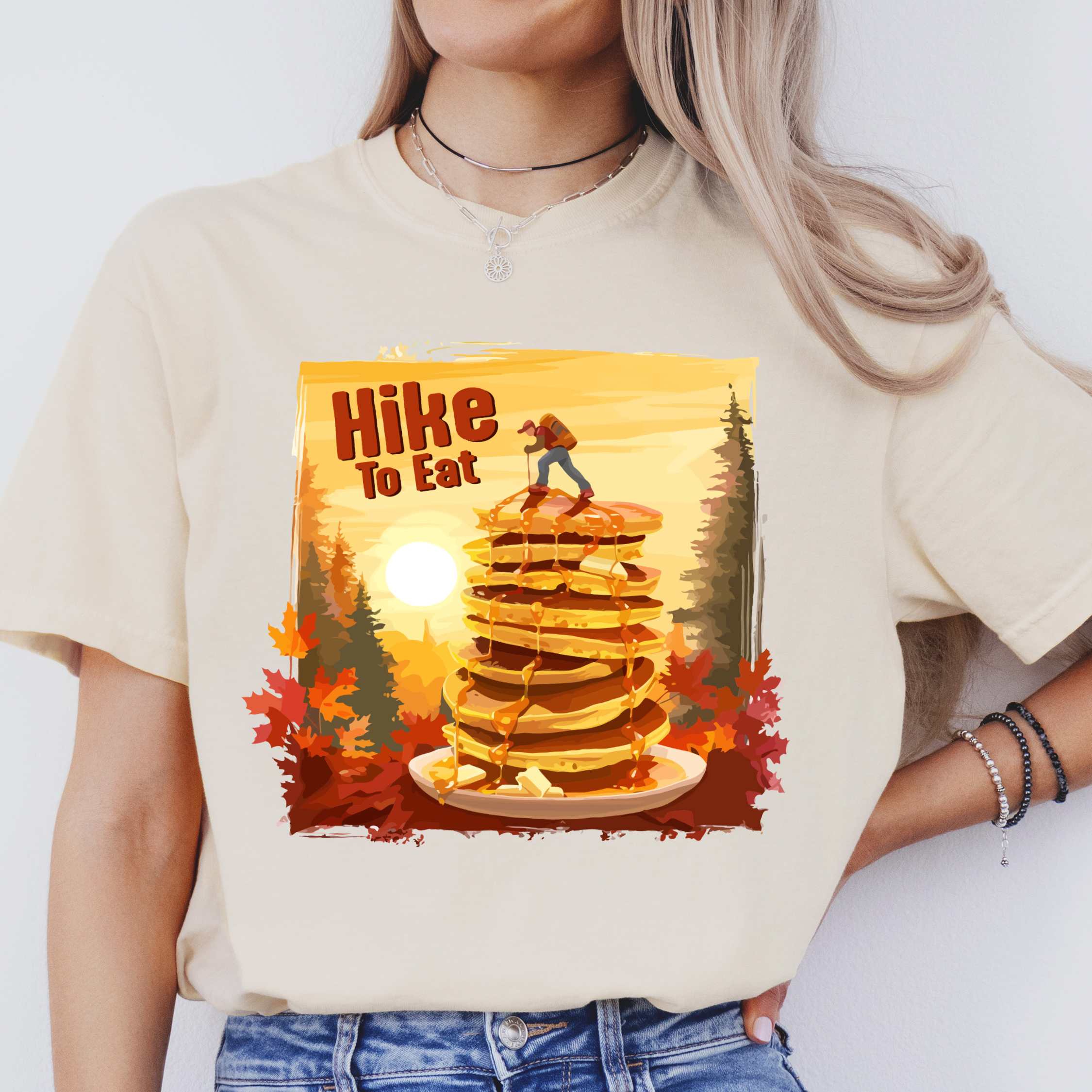 Woman wearing ivory "Hike to Eat" colored vintage statement tee with text in bold lettering, mountains, birds, silhouette, illustrated stack of pancake, and perfect for breakfast lovers.