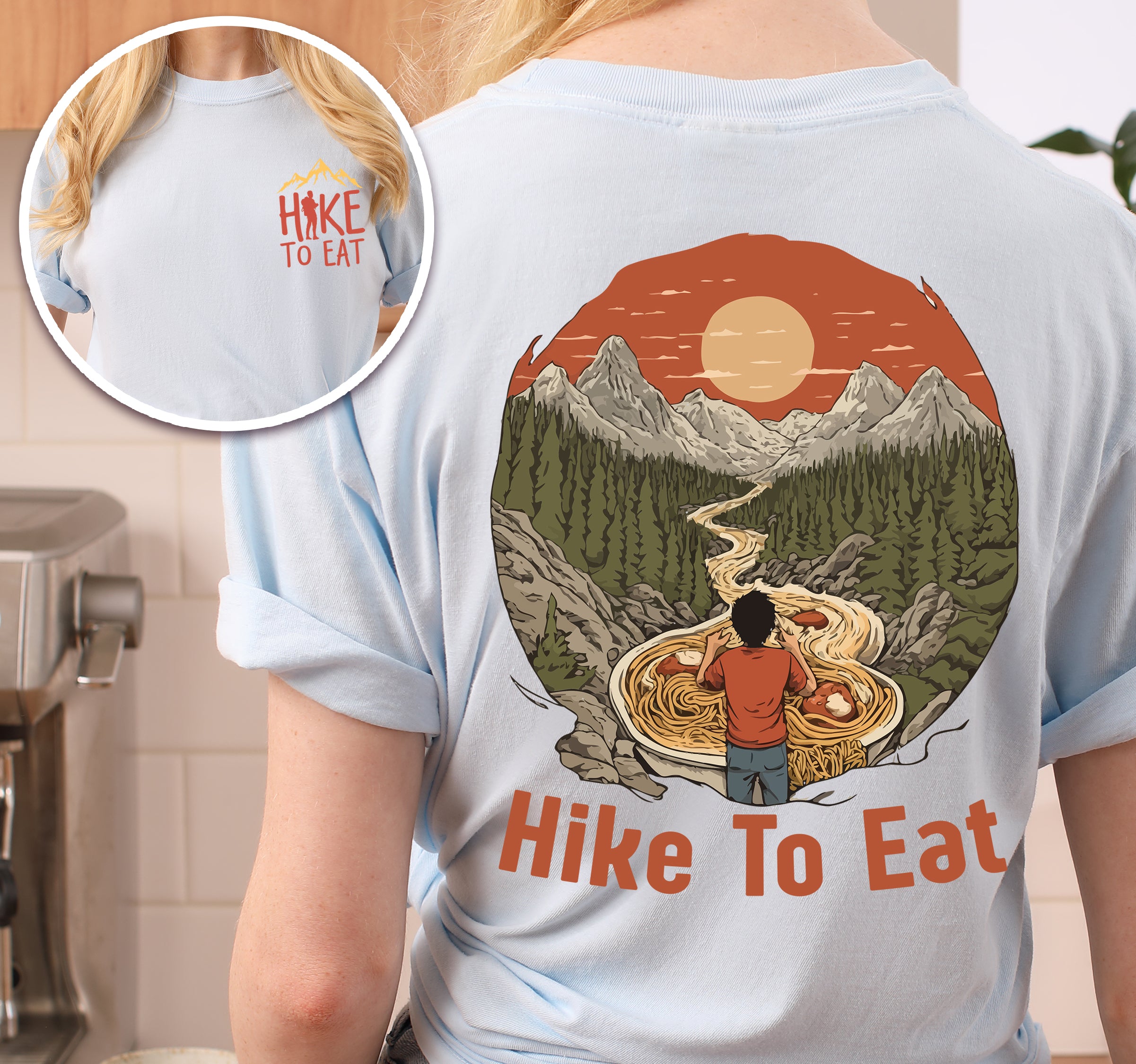 Chambray (Light Blue) Hike to Eat t-shirt front and back view showing small colorful chest detail and large back design featuring hiker standing by steaming bowl of noodles in circular mountain landscape with orange sunset and winding trail.