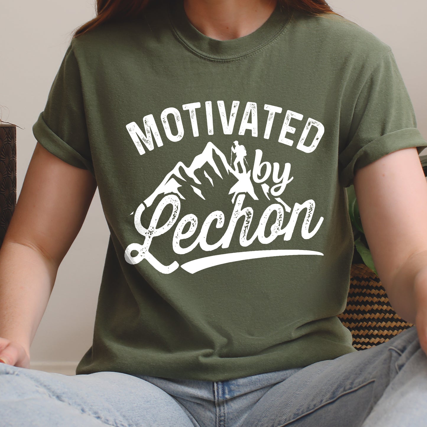Moss (Dark Green) graphic t-shirt with 'Motivated by Lechon' text in white lettering featuring mountain silhouettes and hiker illustration