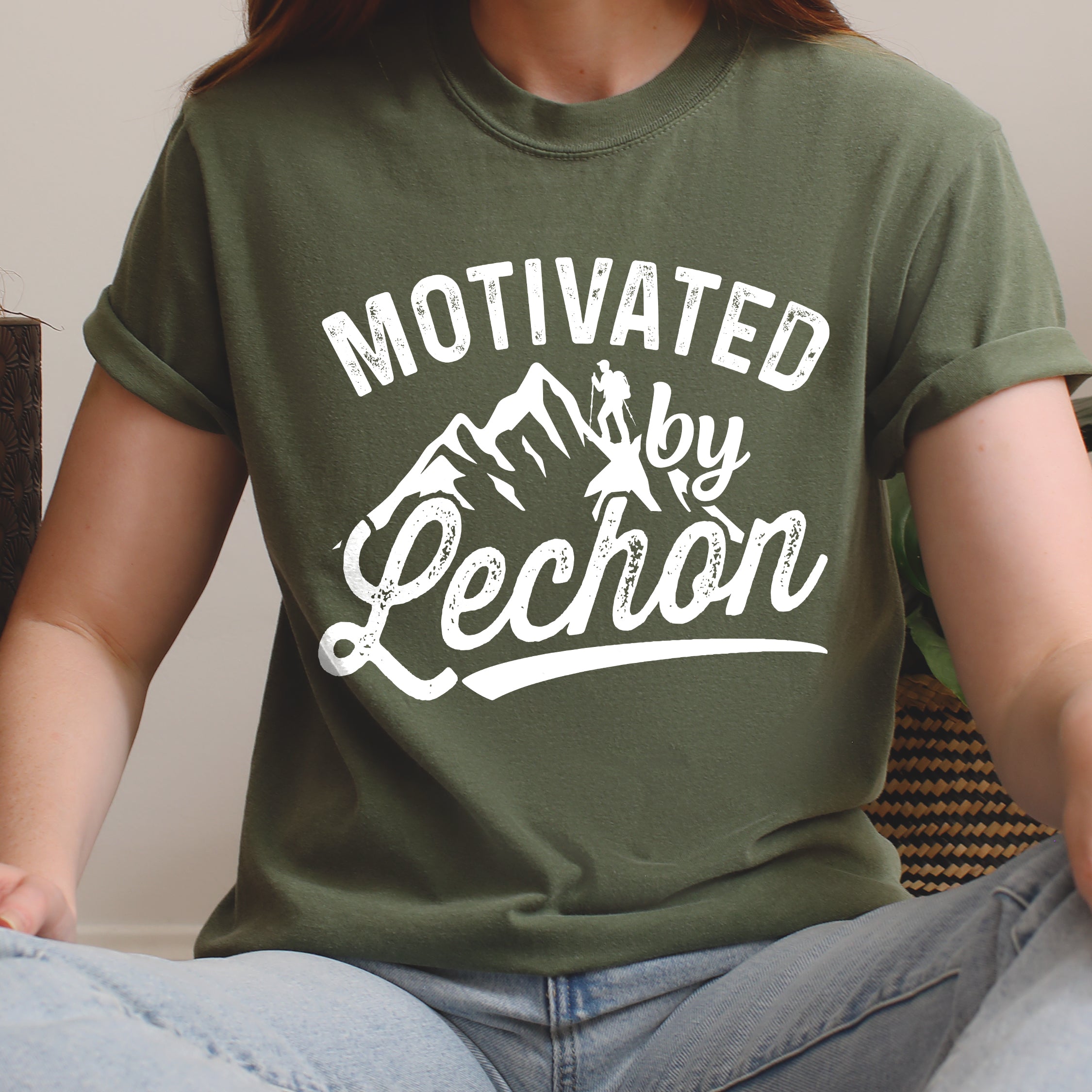 Moss (Dark Green) graphic t-shirt with 'Motivated by Lechon' text in white lettering featuring mountain silhouettes and hiker illustration