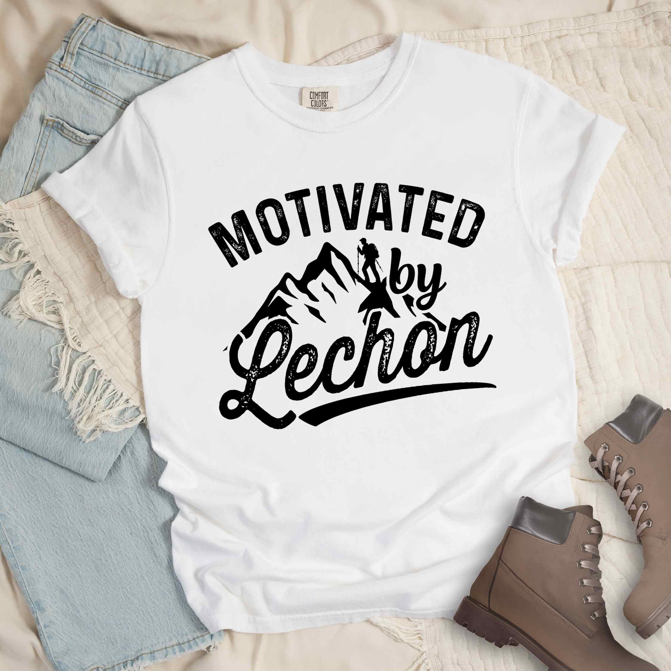 White colored graphic t-shirt with 'Motivated by Lechon' text in white lettering featuring mountain silhouettes and hiker illustration