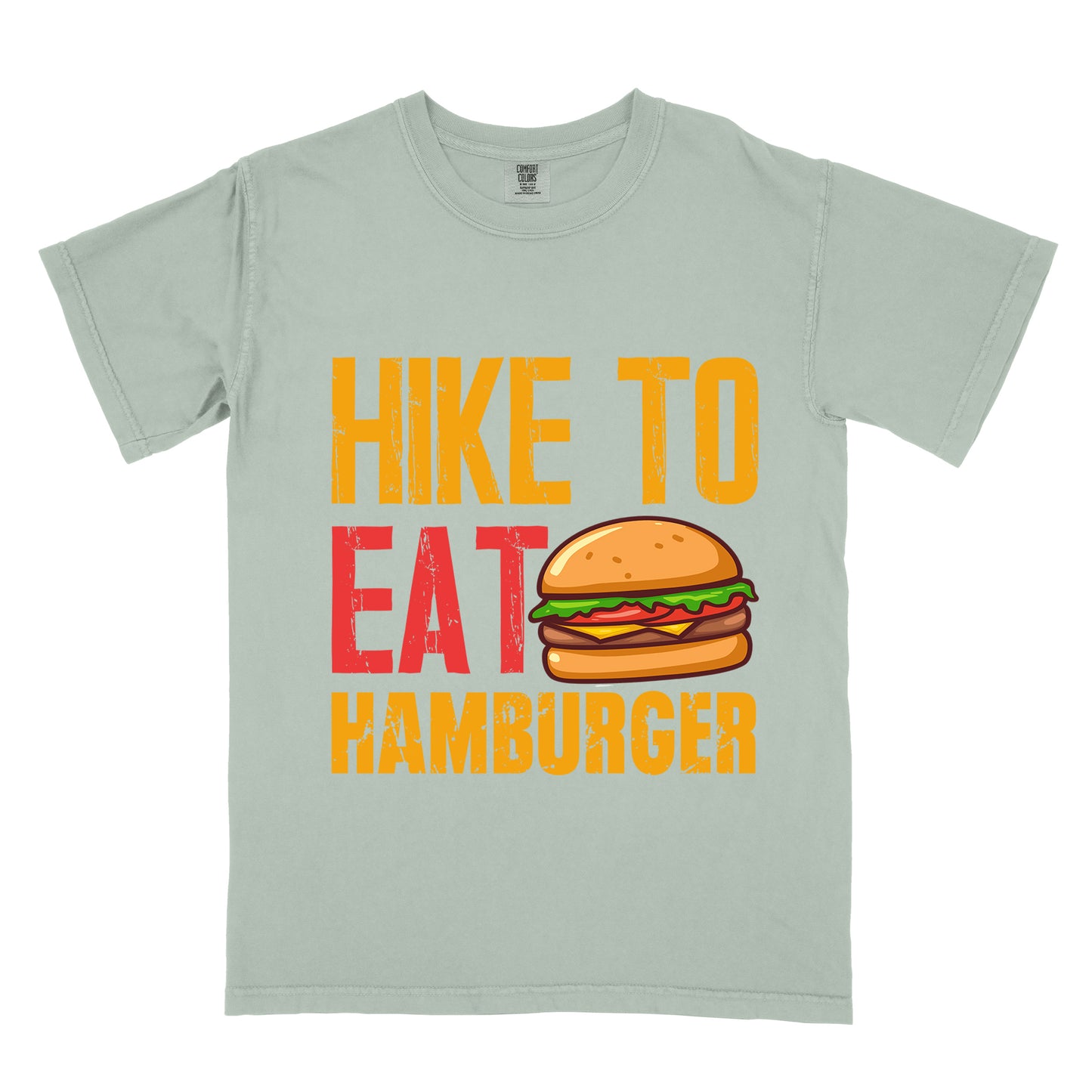 Bay (Light Gray) t-shirt with distressed text reading "HIKE TO EAT HAMBURGER" arranged in three lines. "HIKE TO" appears in yellow at the top, "EAT" in red in the middle with a colorful hamburger illustration next to it, and "HAMBURGER" in yellow at the bottom. The hamburger graphic shows a bun, meat patty, cheese, lettuce, and tomato.