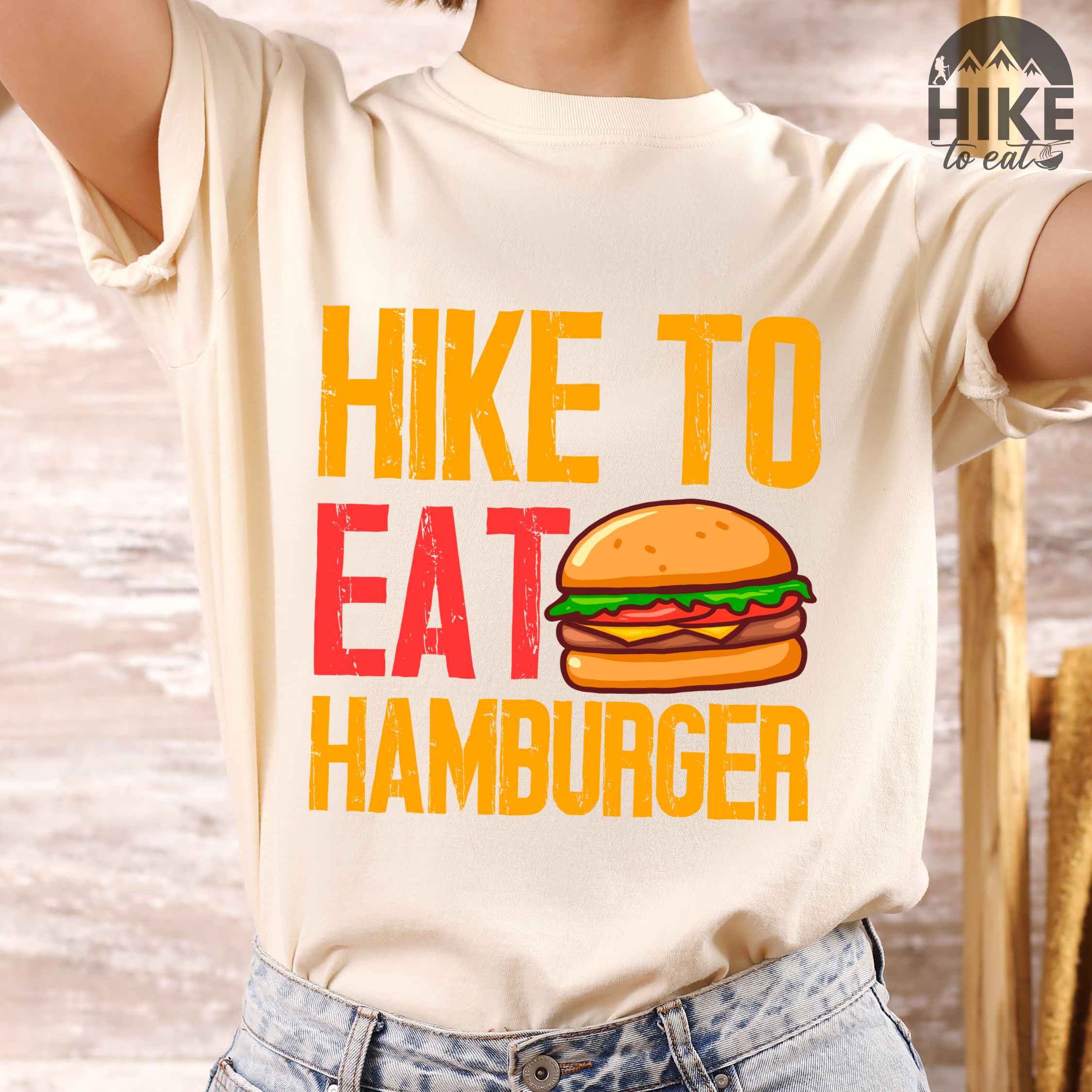 Woman wearing ivory "Hike to eat Hamburger" colored vintage tee with bold typography, juicy cheese hamburger illustration, perfect for the hamburger enthusiasts.