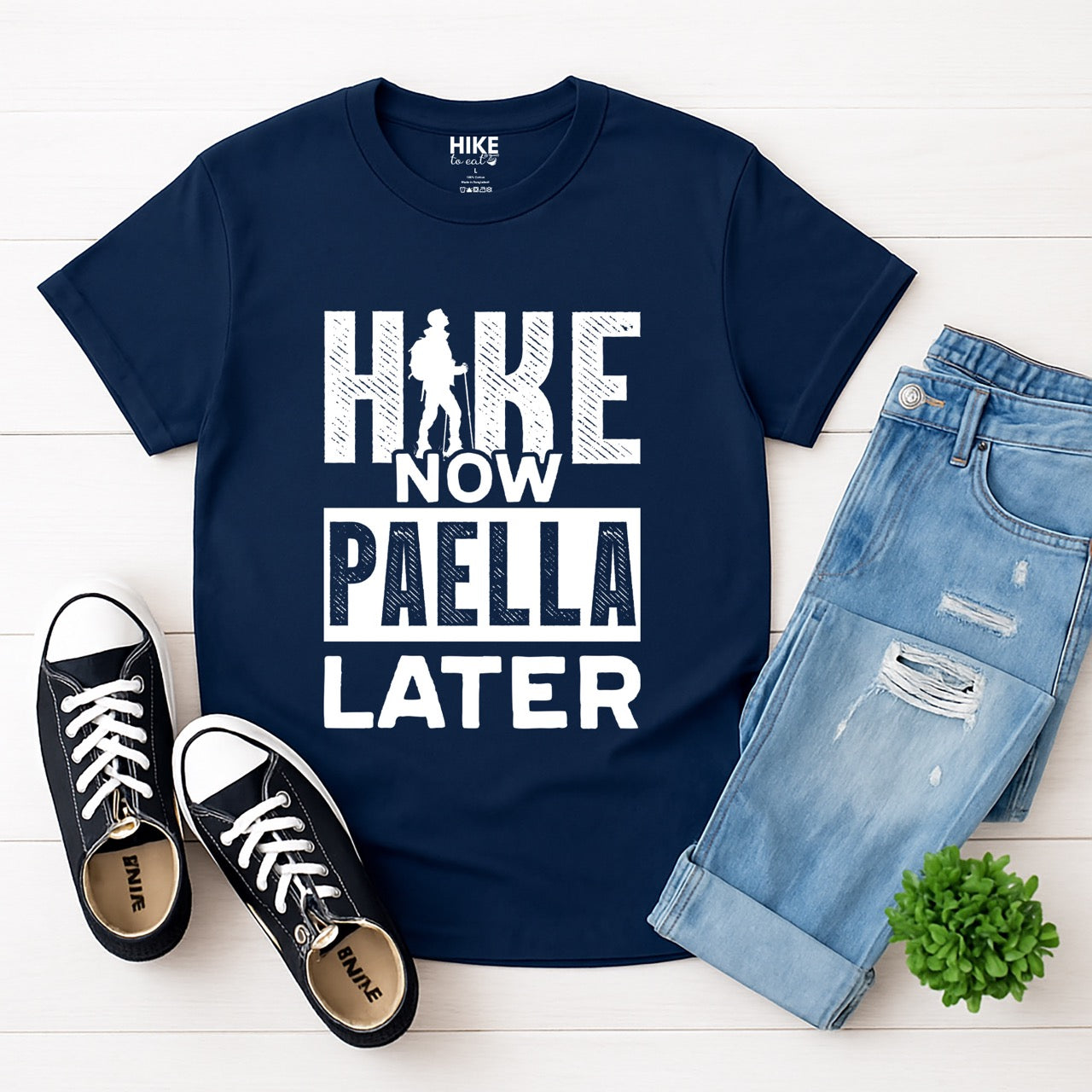 navy blue Hike Now Paella Later statement tee with bold distressed typography and hiker silhouette for Spanish food-loving outdoor enthusiasts and hikers with jeans and shoes