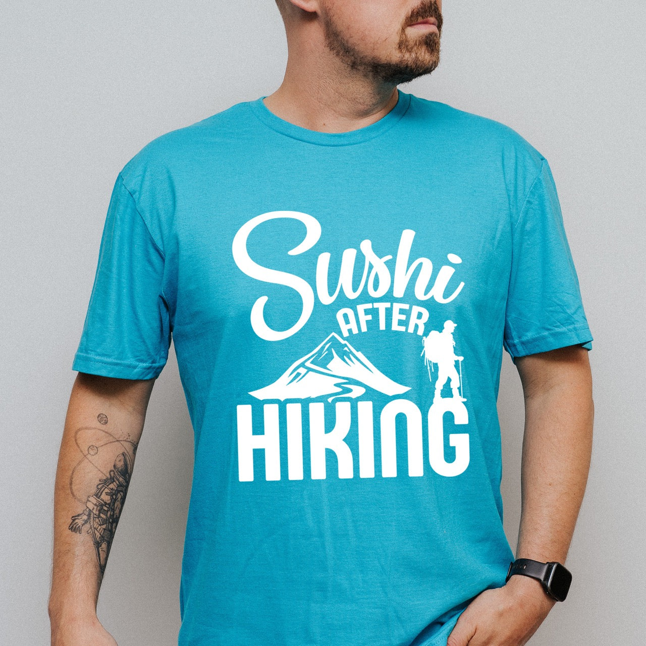man wearing tropical blue Sushi after Hiking statement tee with elegant script typography, mountain peaks, and hiker silhouette for Japanese food-loving outdoor enthusiasts , foodies and hikers