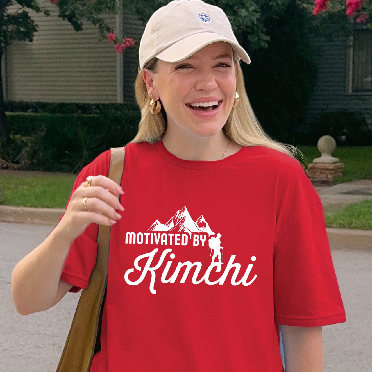 woman smiling while wearing red Motivated by Kimchi statement tee with bold typography, elegant script lettering, mountain peaks, and hiker silhouette for Korean food-loving outdoor enthusiasts, foodies and hikers