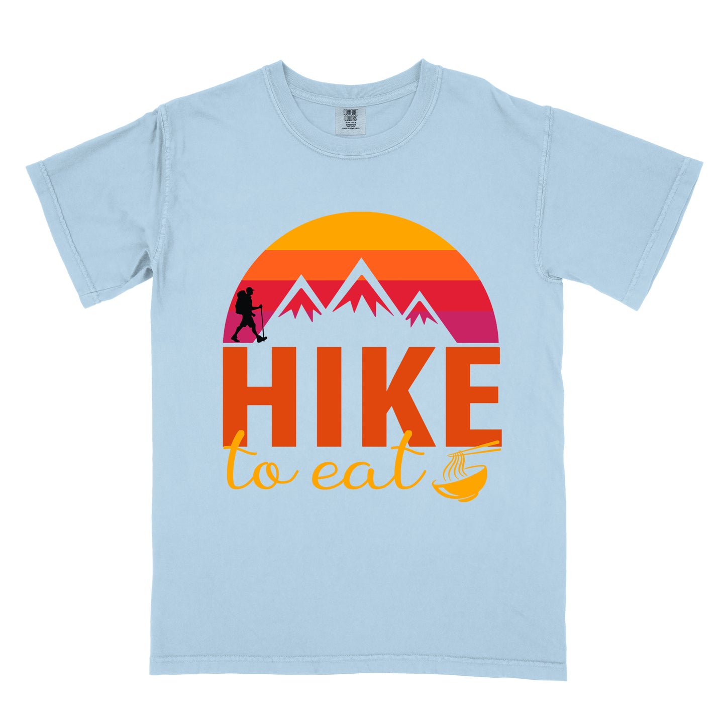 Chambray (Light Blue) t-shirt featuring a retro sunset design with gradient colors from yellow to orange to red to purple. Mountain silhouettes and a small hiker figure appear against the sunset. Below this is "HIKE" in large orange letters and "to eat" in yellow script, followed by a small illustration of a noodle bowl with chopsticks. The design has a vintage outdoor aesthetic.